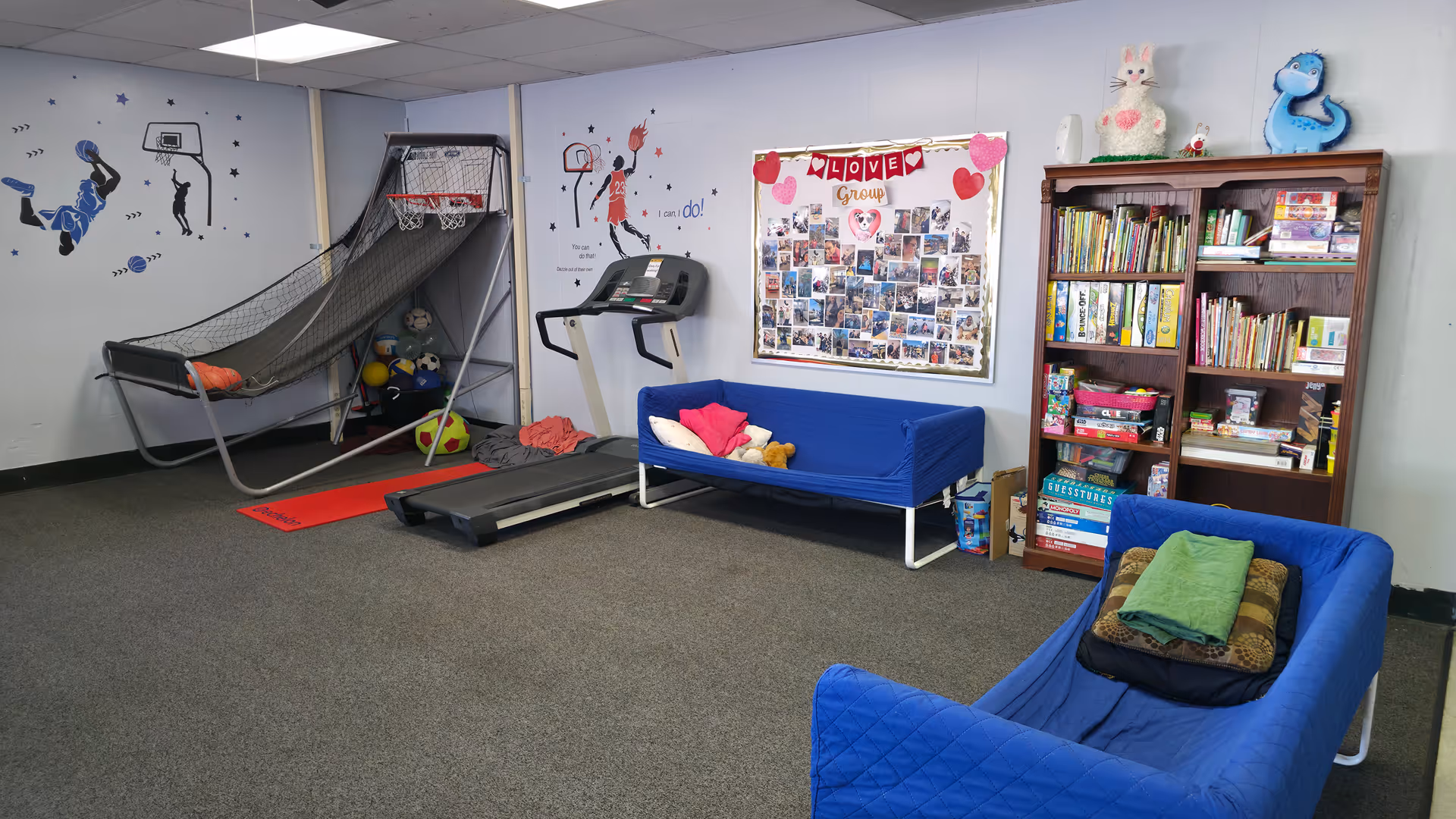 Indoor activity room with a treadmill, blue couches, and a bookshelf.