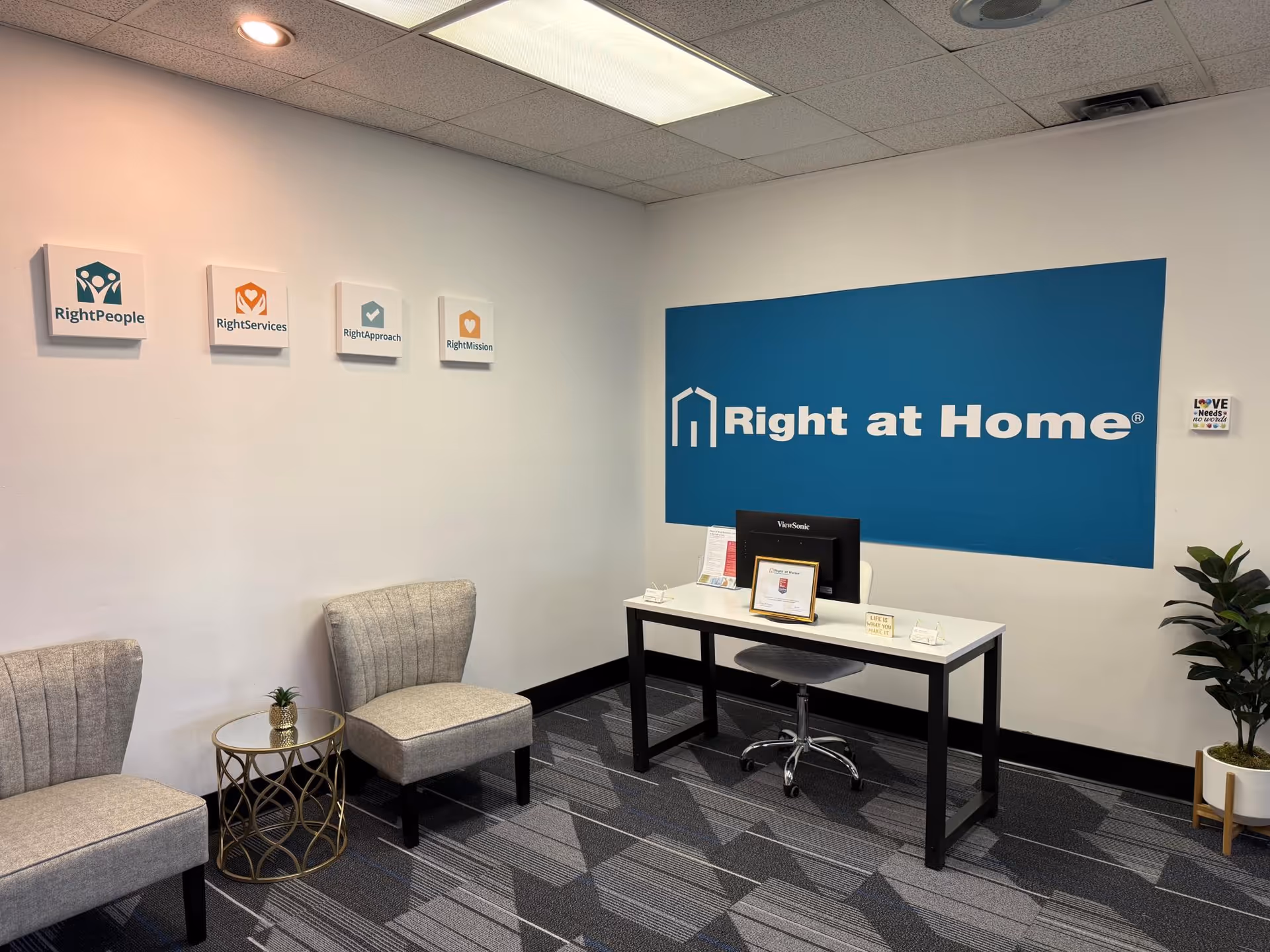 Office reception area with a desk, blue Right at Home sign, and seating.