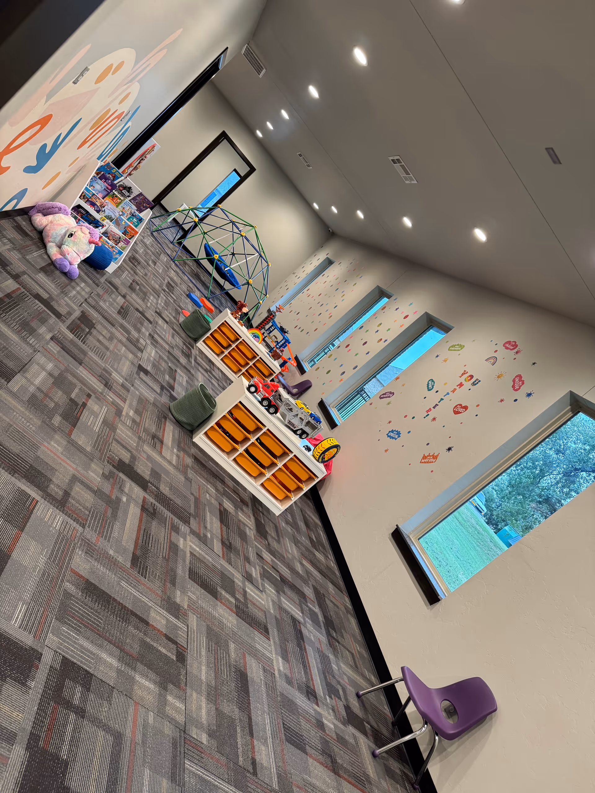 Colorful indoor playroom with toy shelves, a geodesic climbing dome, and wall decals.