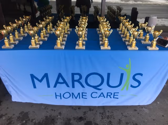 Award table displaying numerous gold trophies with Marquis Home Care branding.