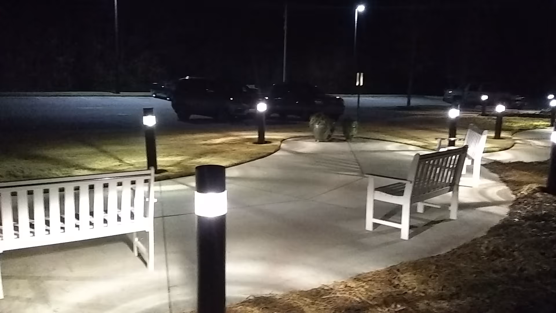 Nighttime outdoor pathway with white benches and illuminated bollard lights.