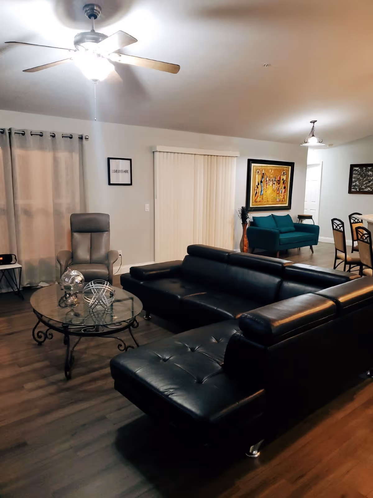 Spacious senior living room with black leather sectional and glass coffee table.