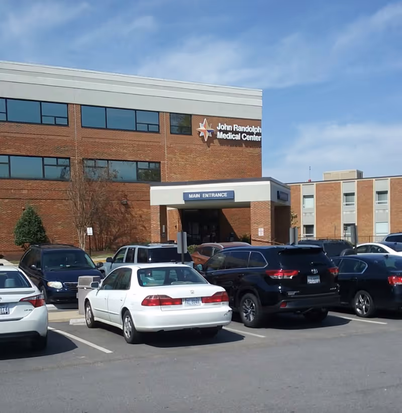 Exterior view of John Randolph Medical Center, brick building with glass windows and parked cars.