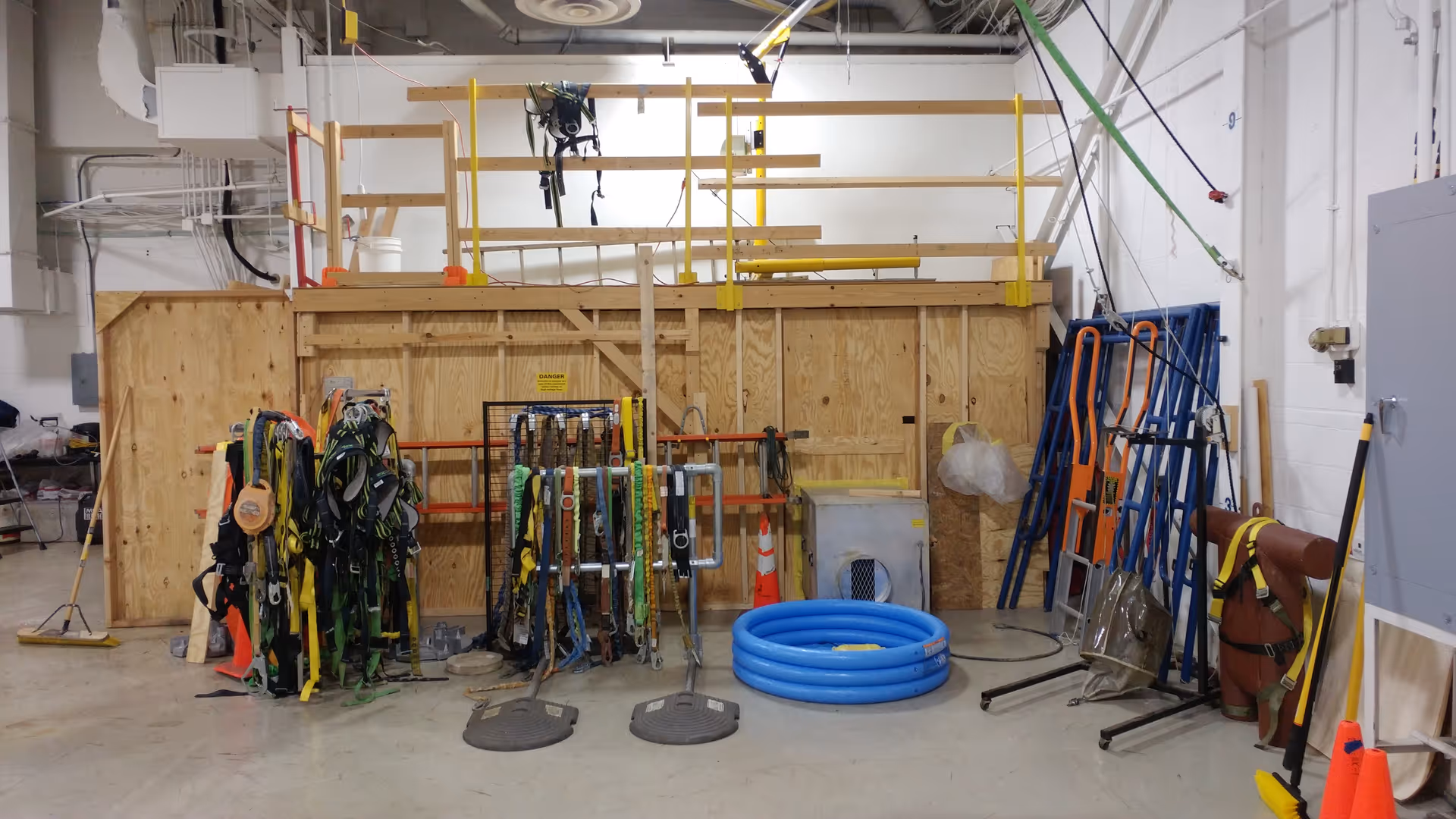 Industrial storage/workshop area filled with harnesses, tools, ladders, and blue hoses.