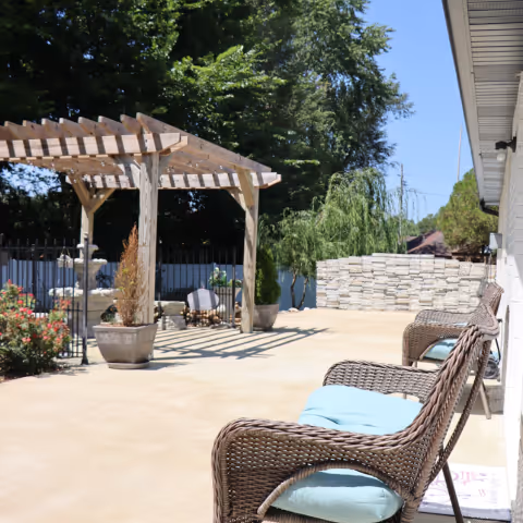 Sunny outdoor patio at Jacob's Houses with wicker chairs, a wooden pergola, and potted plants.