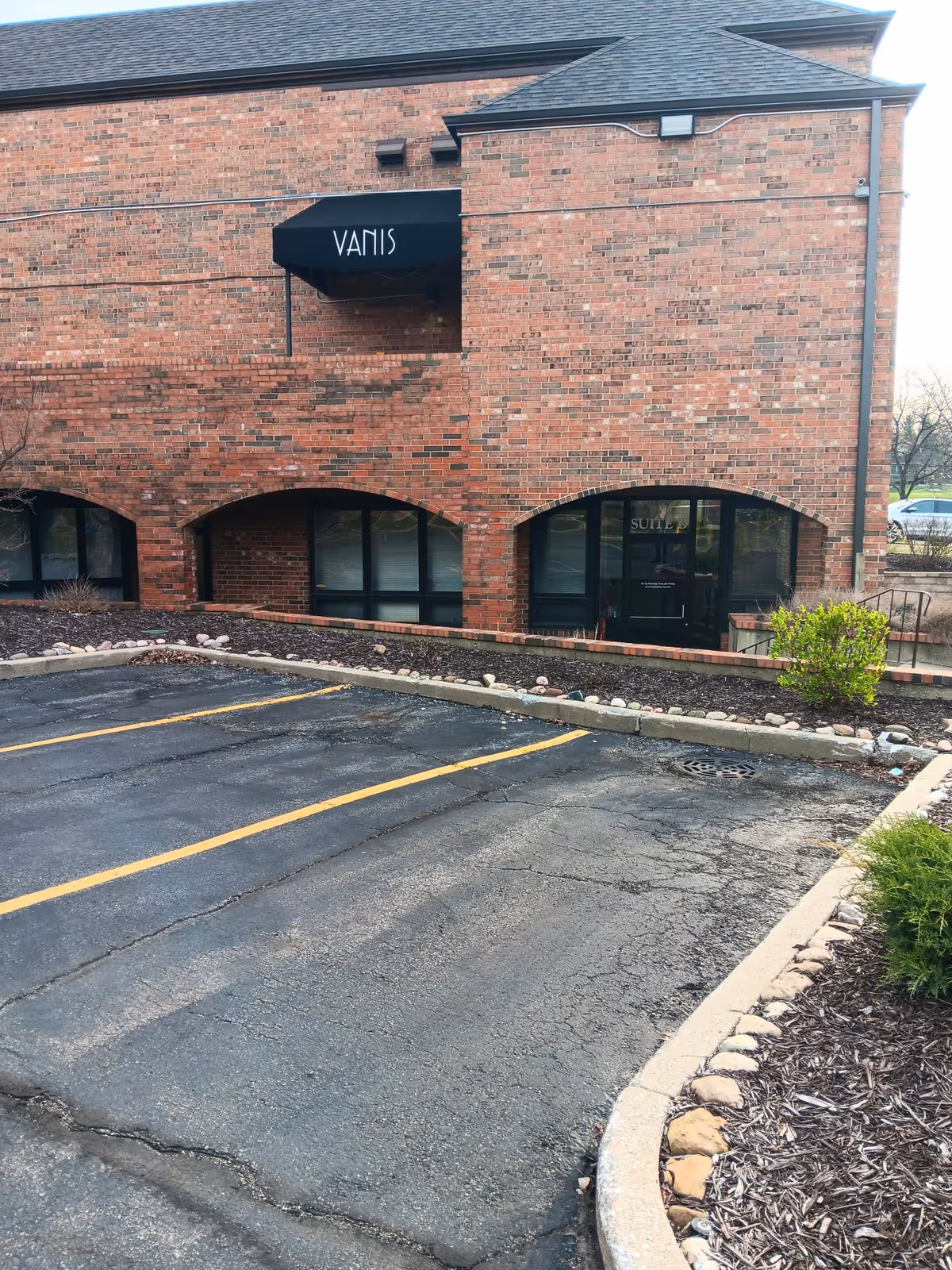 Brick building with a black awning sign reading VANIS over a parking lot.