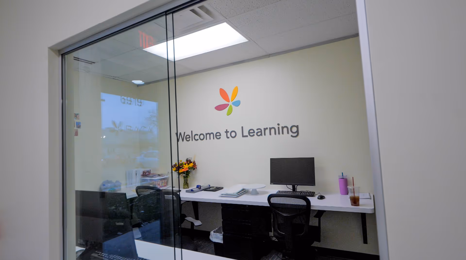 Glass-walled learning office with a desk, computer, and Welcome to Learning sign.