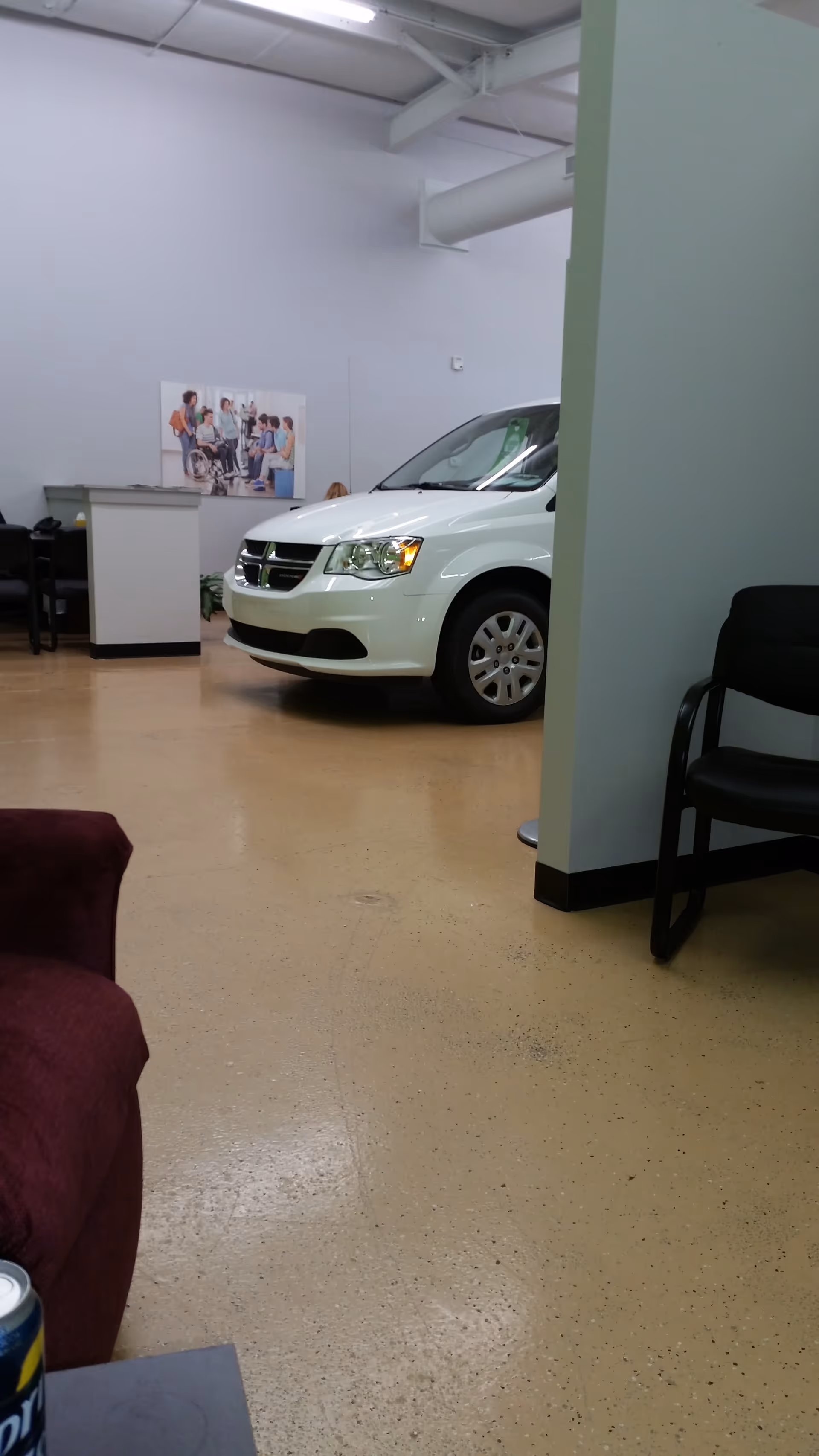 White van displayed inside a bright facility showroom with seating and a poster on the wall.
