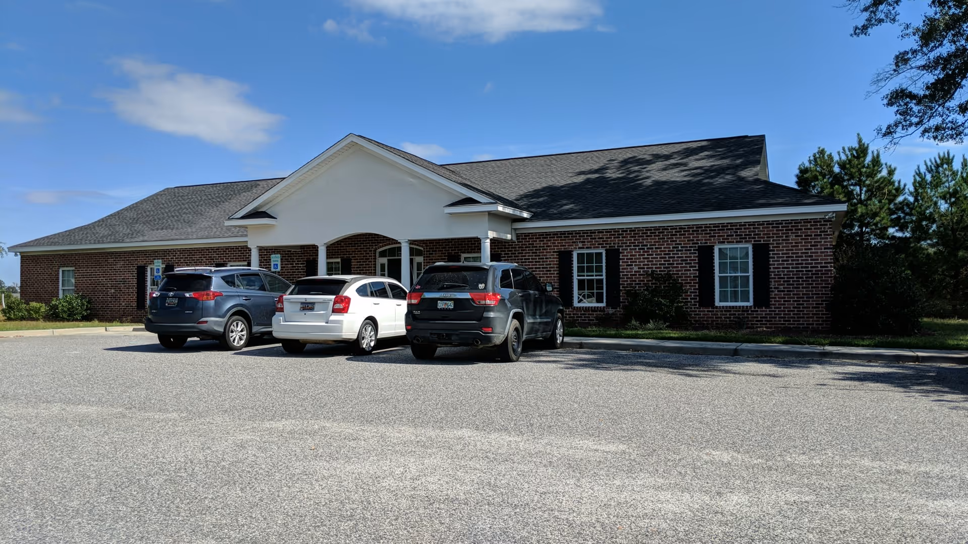 Brick facility with a porte-cochère entrance and several cars parked in front.