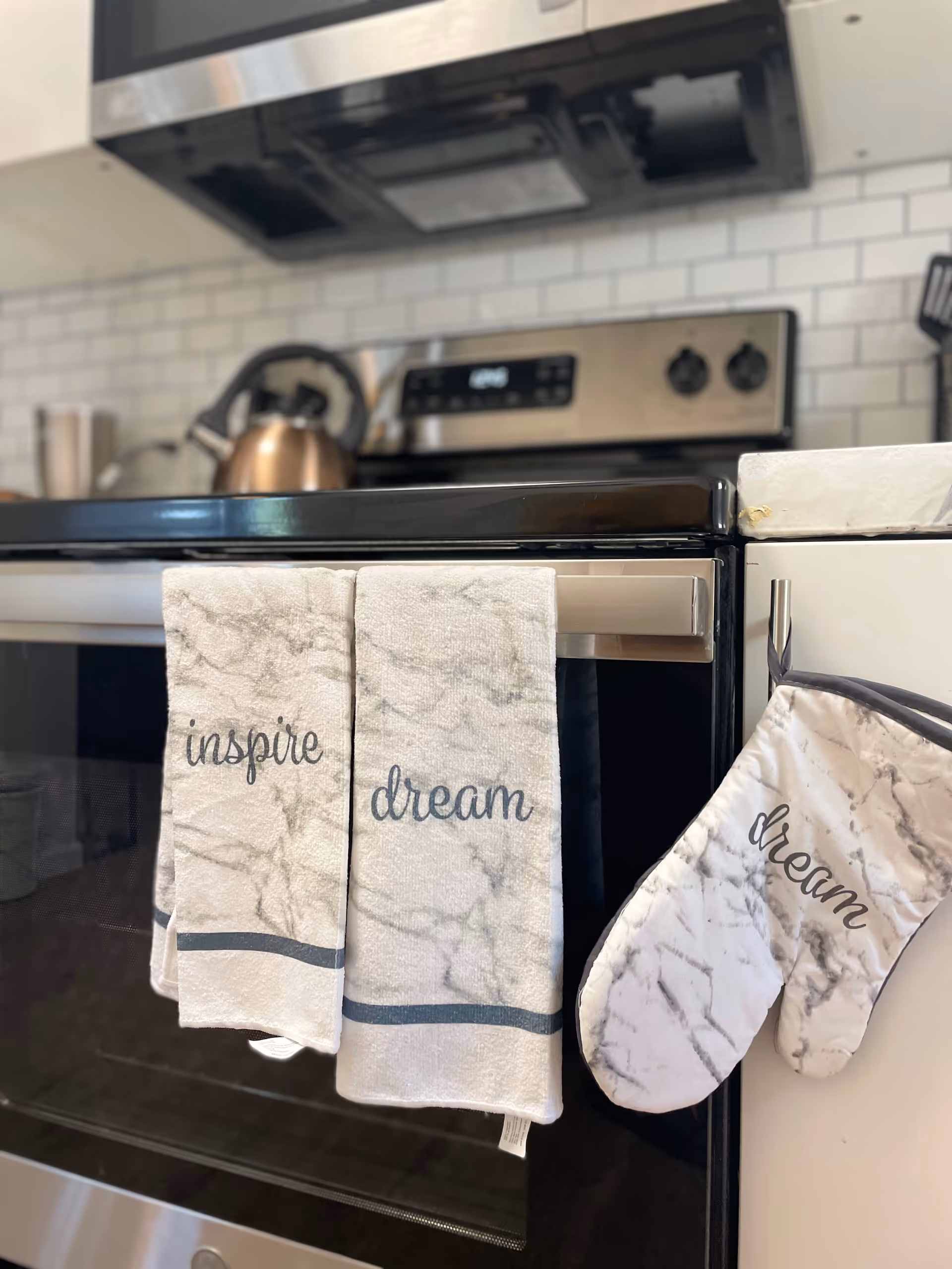 Towels and a marble-patterned oven mitt hang on a stainless steel kitchen stove.