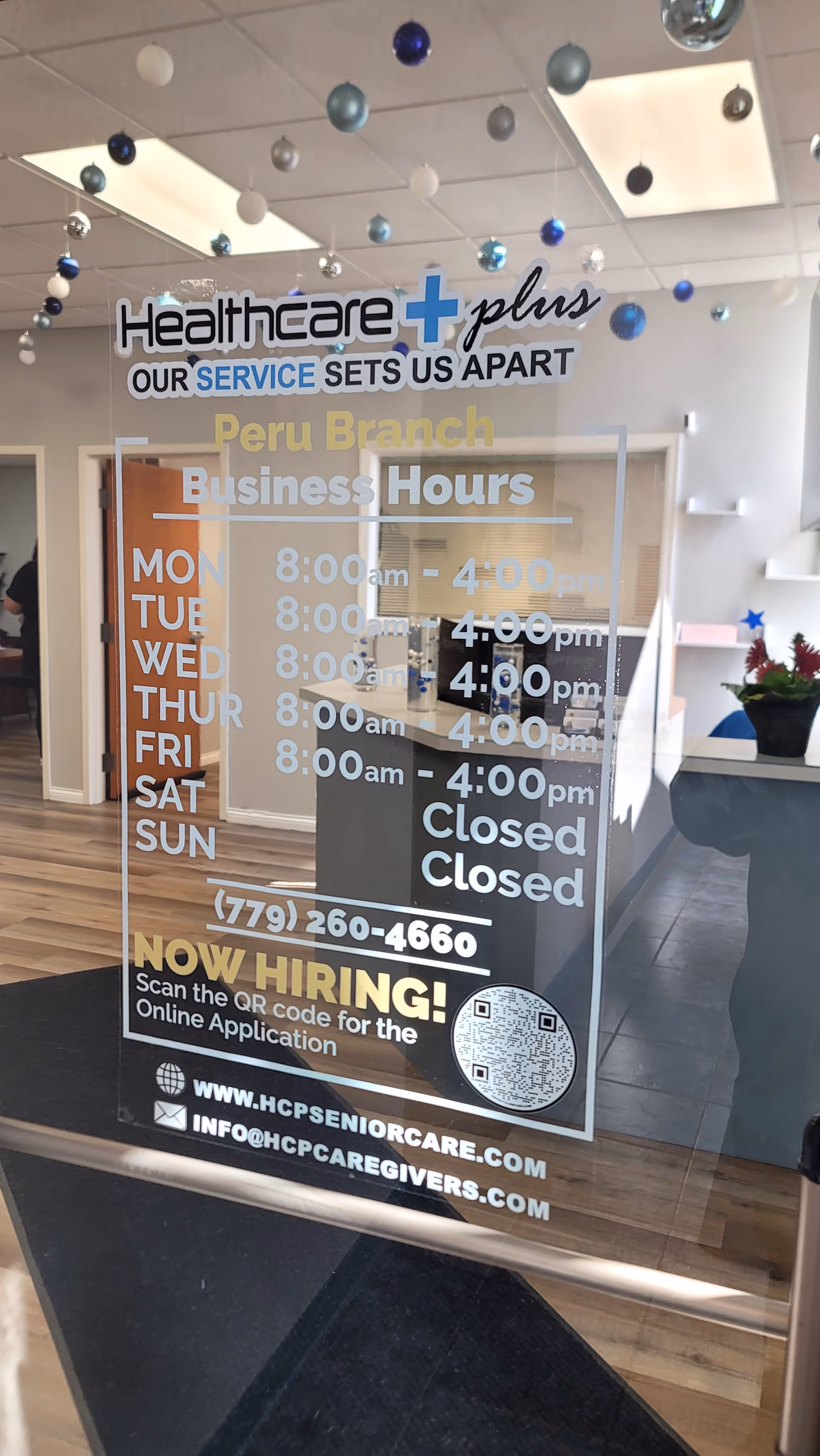 Glass door displays Healthcare Plus Caregivers branch hours, hiring info, and contact details inside.