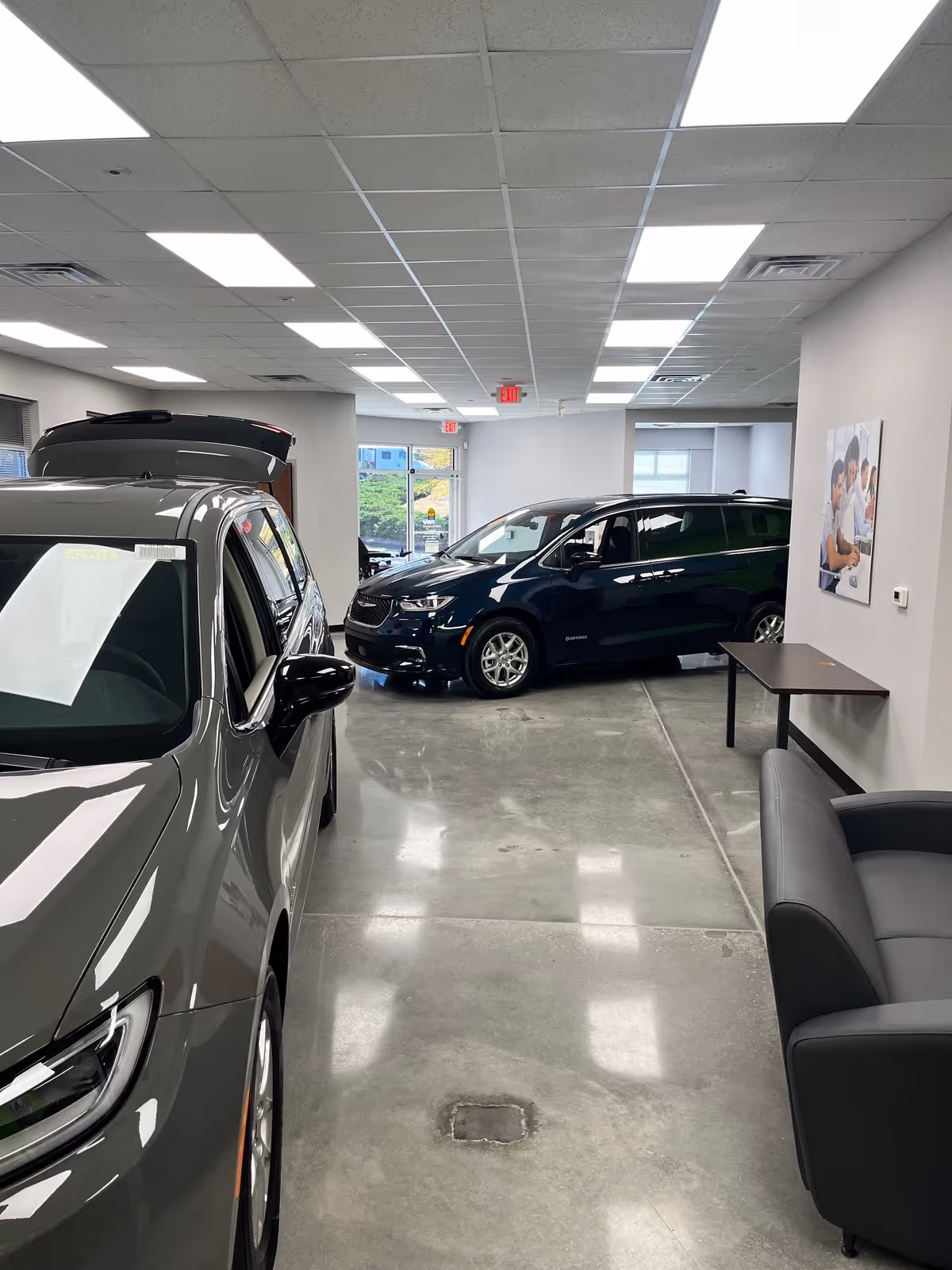Indoor showroom with parked minivans, bright ceiling lights, and a seating area along the wall.