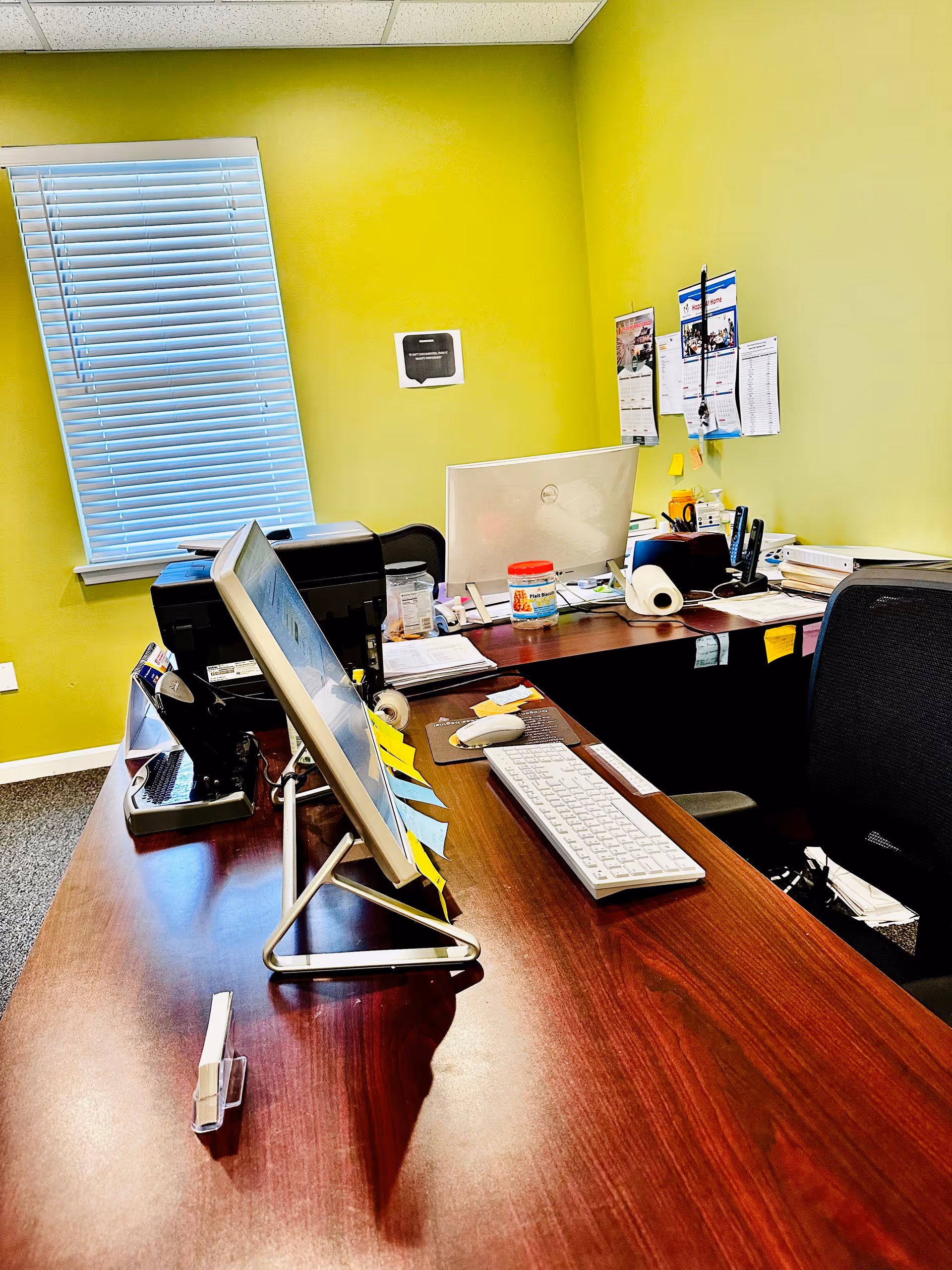Bright lime-green office interior with desks, computers, and scattered papers.