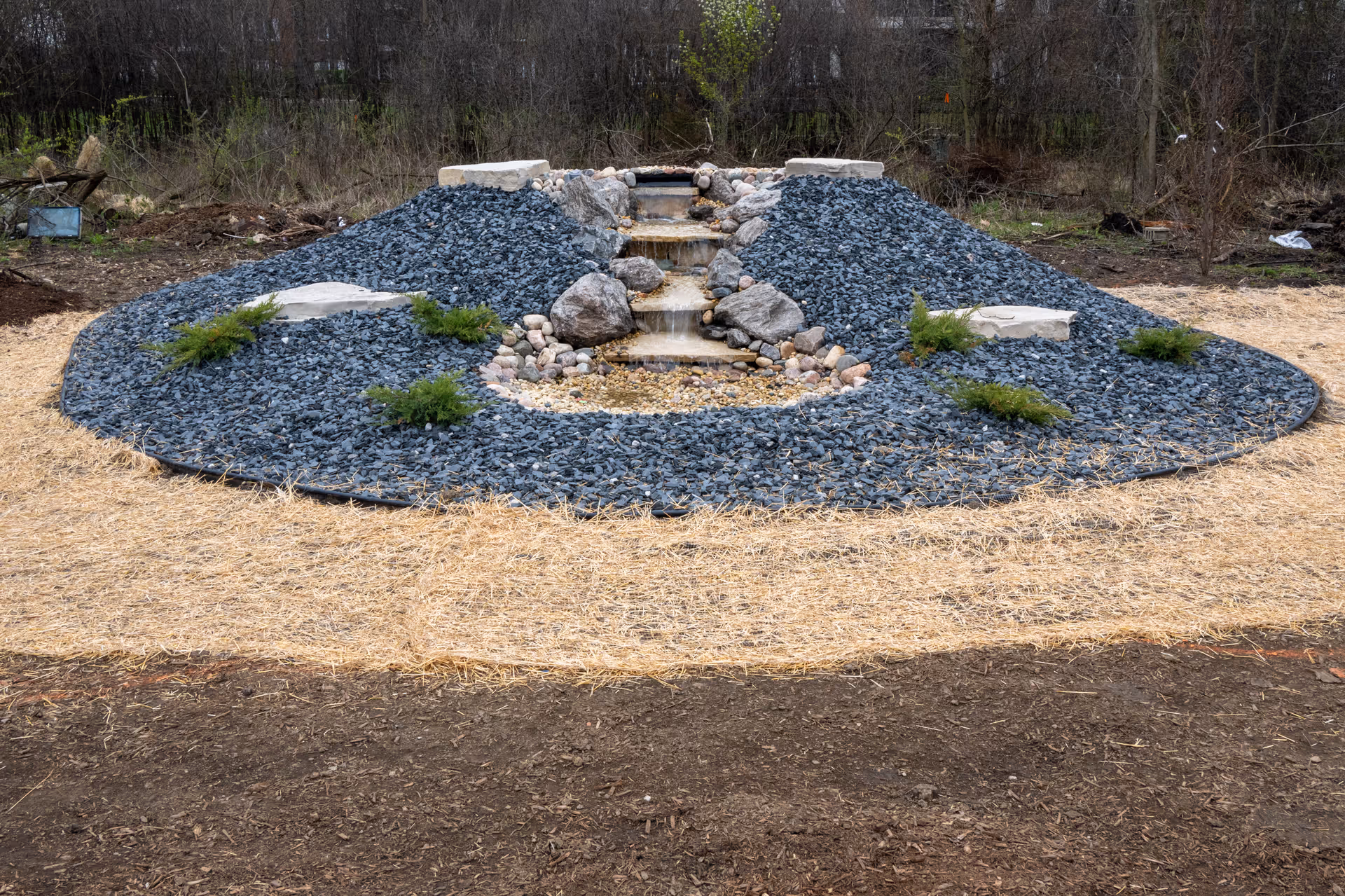 A circular outdoor rock garden features stone steps and a small waterfall.