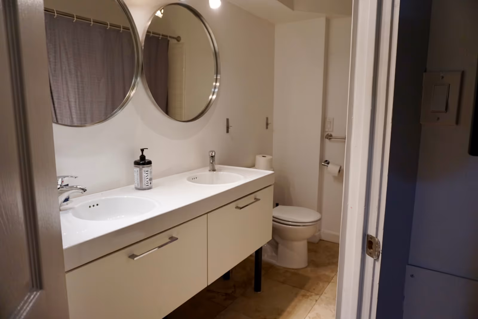 Modern bathroom with double sinks, round mirrors, and a toilet.