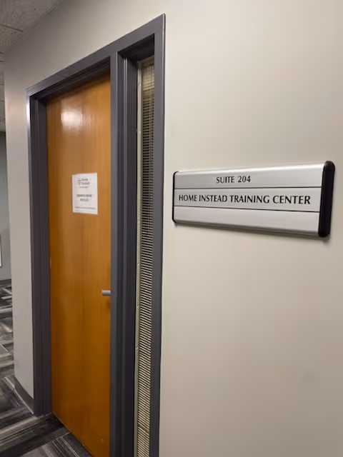 Interior hallway with a wooden door and a sign reading Home Instead Training Center Suite 204.