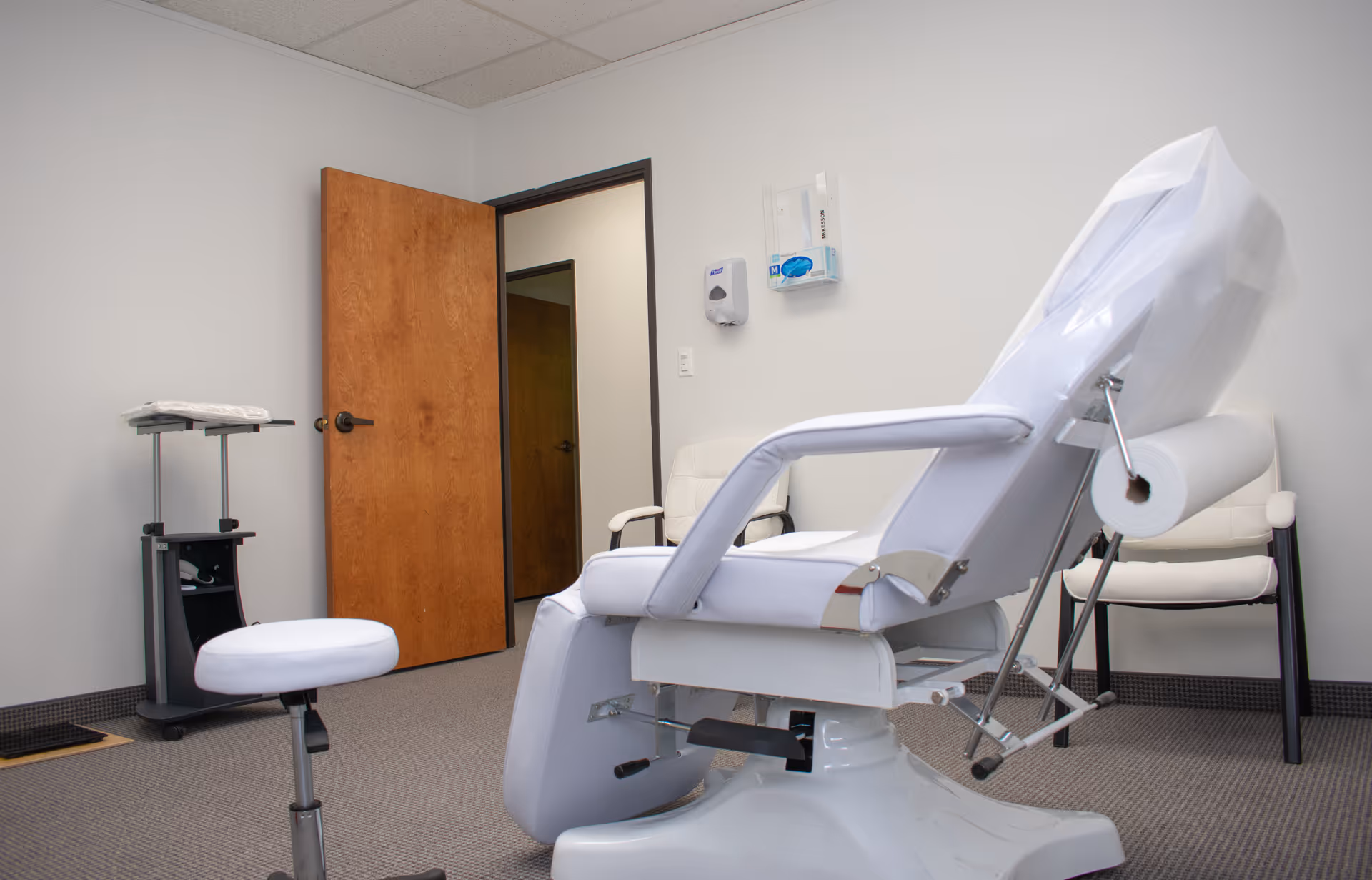 Medical examination chair in a small clinic room with a wooden door.
