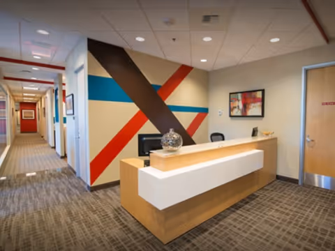 Modern reception desk in a hallway with colorful geometric wall art and neutral carpet.