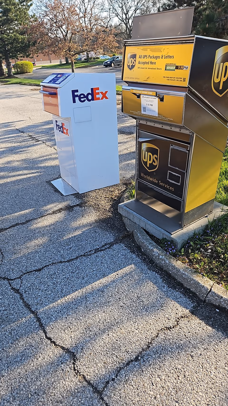 Outdoor row of FedEx and UPS mailboxes beside a parking lot.