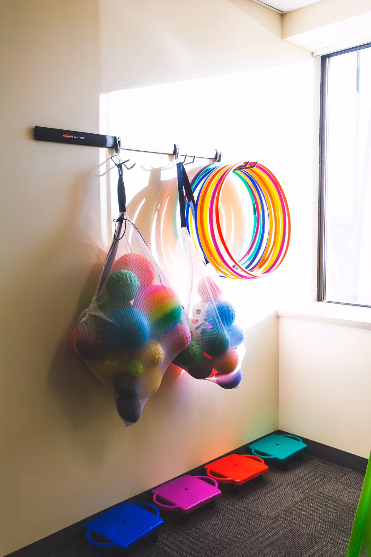 Colorful therapy toys and rainbow hoops hung on a wall in a small play area.