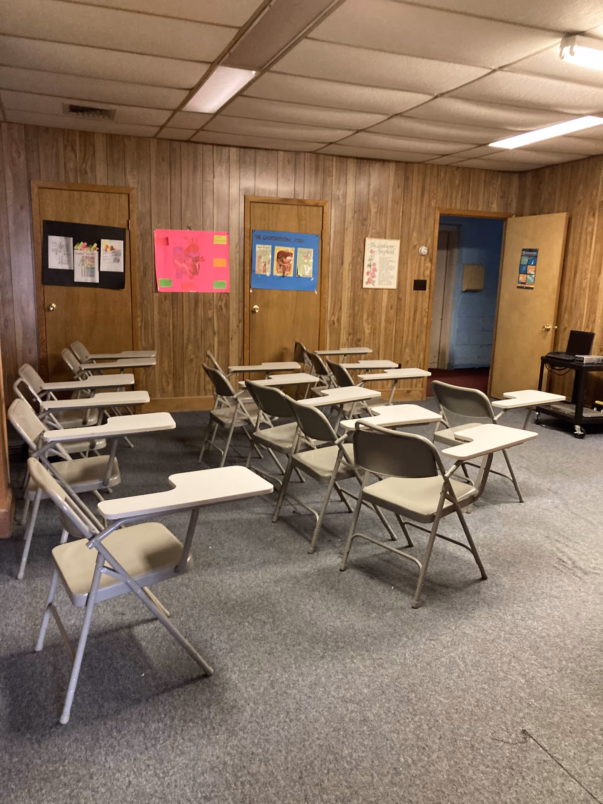 Wood-paneled classroom area with rows of folding desks and posters on walls
