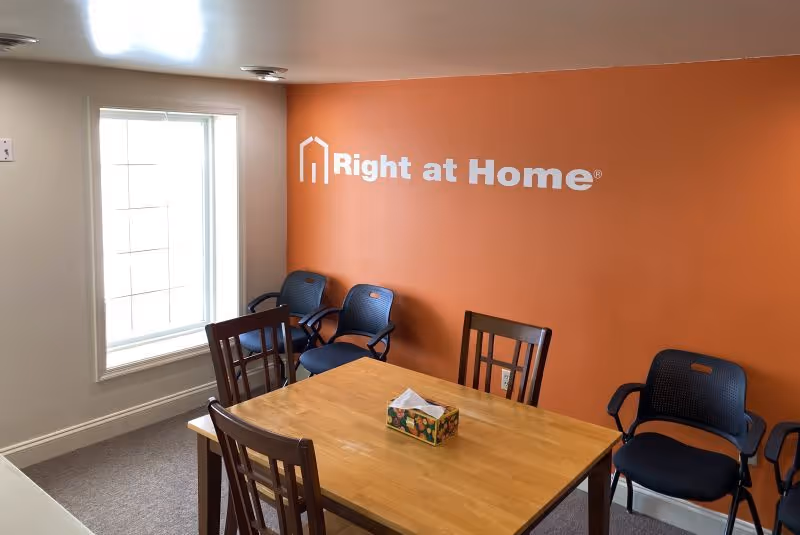 Interior dining area with orange wall logo, wooden table, and several chairs.