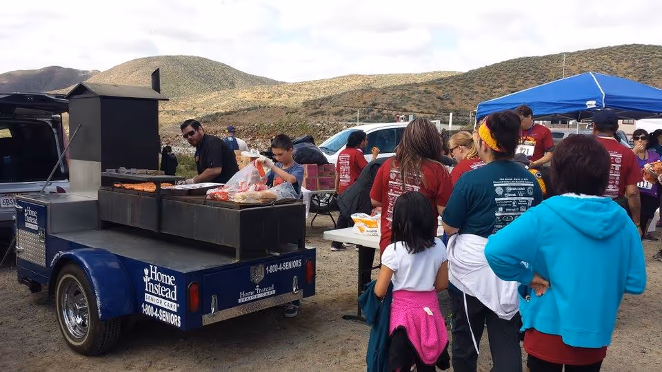 Outdoor scene with a Home Instead food truck and volunteers assisting attendees.