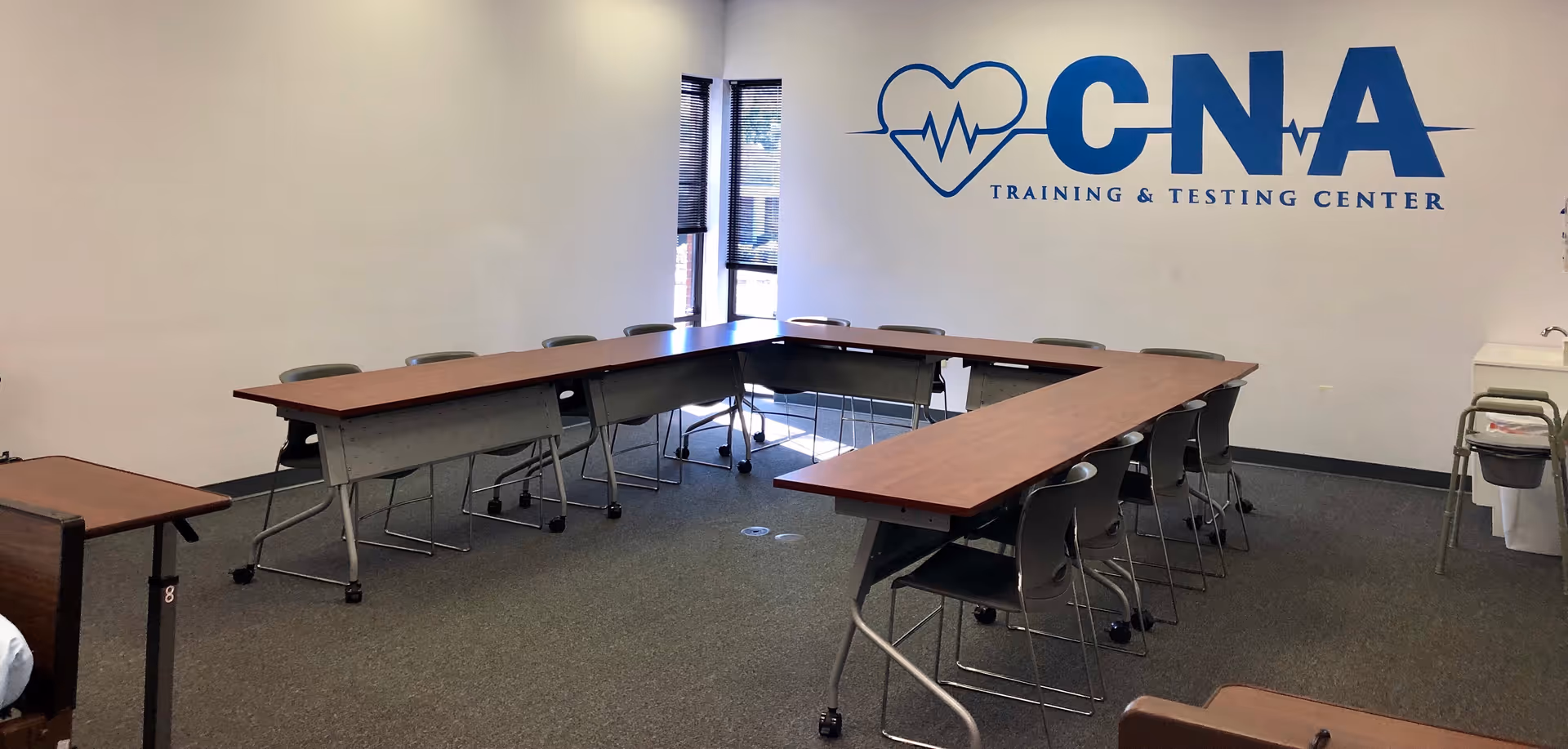 A U-shaped conference room setup with tables and chairs, displaying CNA Training and Testing Center logo.