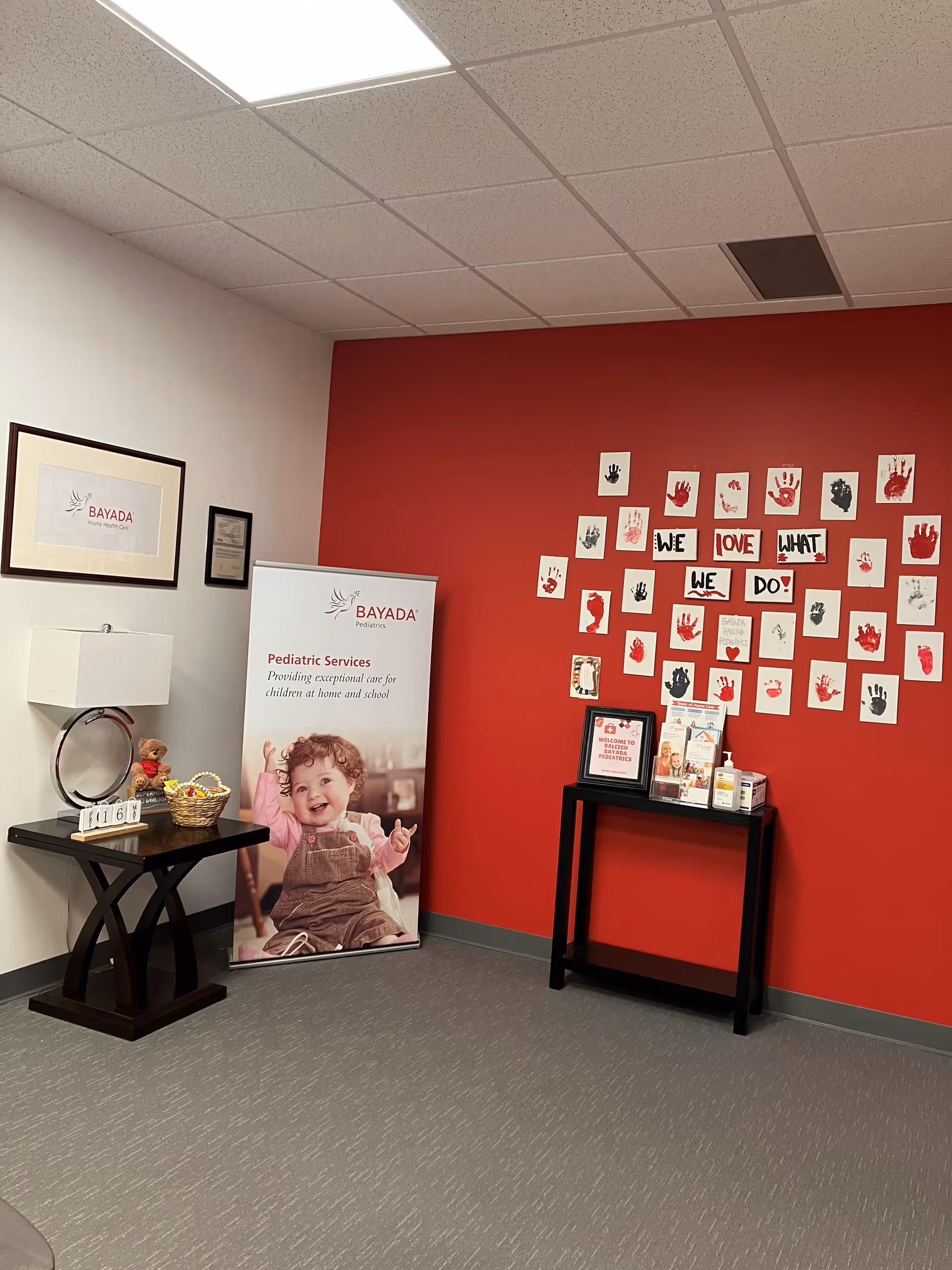 Interior lobby area with a red wall art, BAYADA banner, tables, and handprint display.