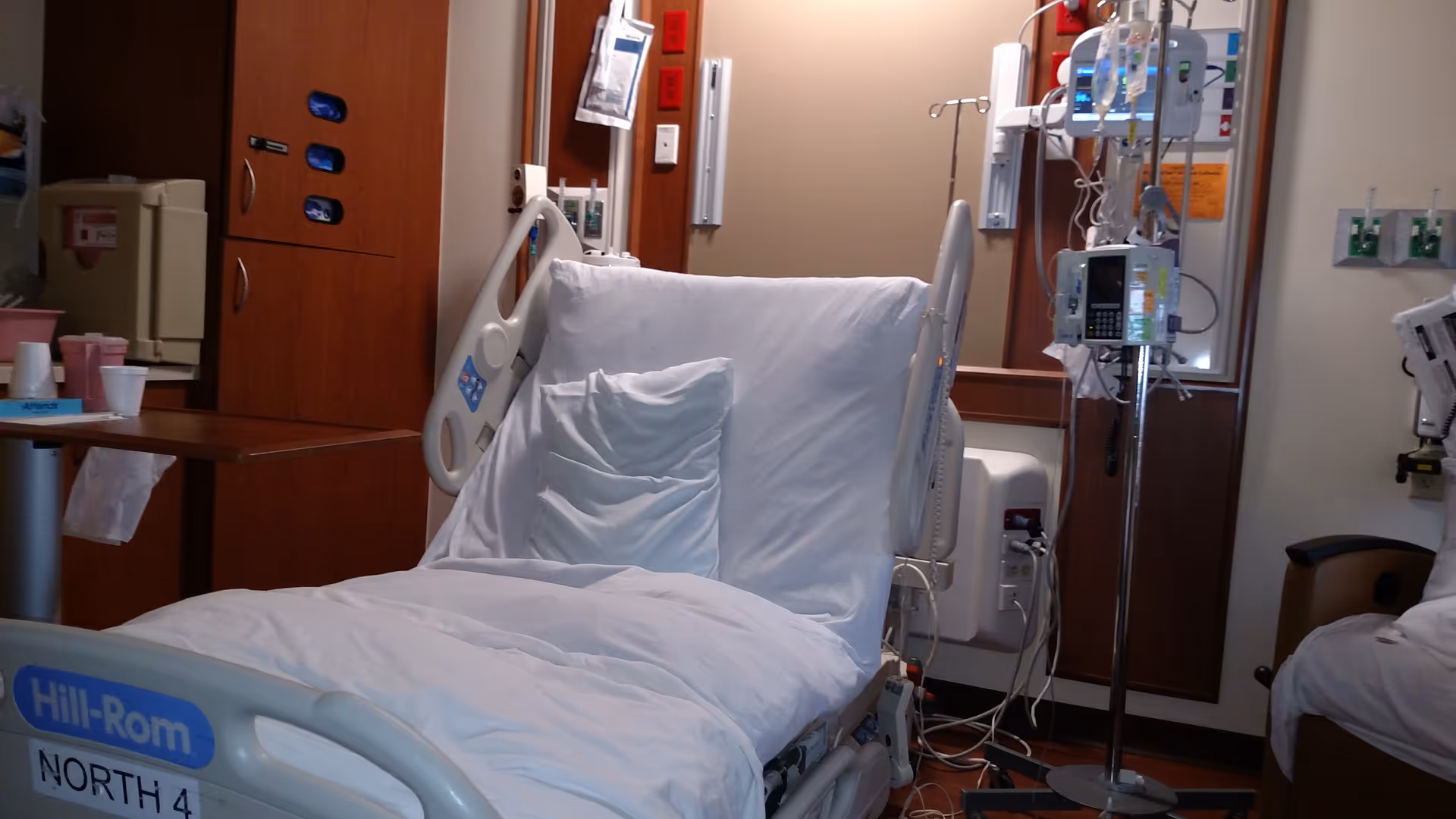 Hospital bed in a patient room with IV poles and monitoring equipment.