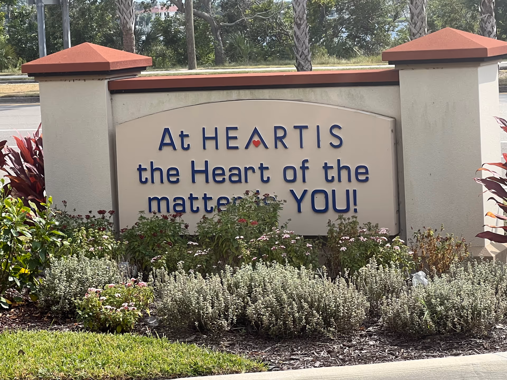 Front entrance sign reading 'At HEARTIS the Heart of the matter YOU!' with landscaping.