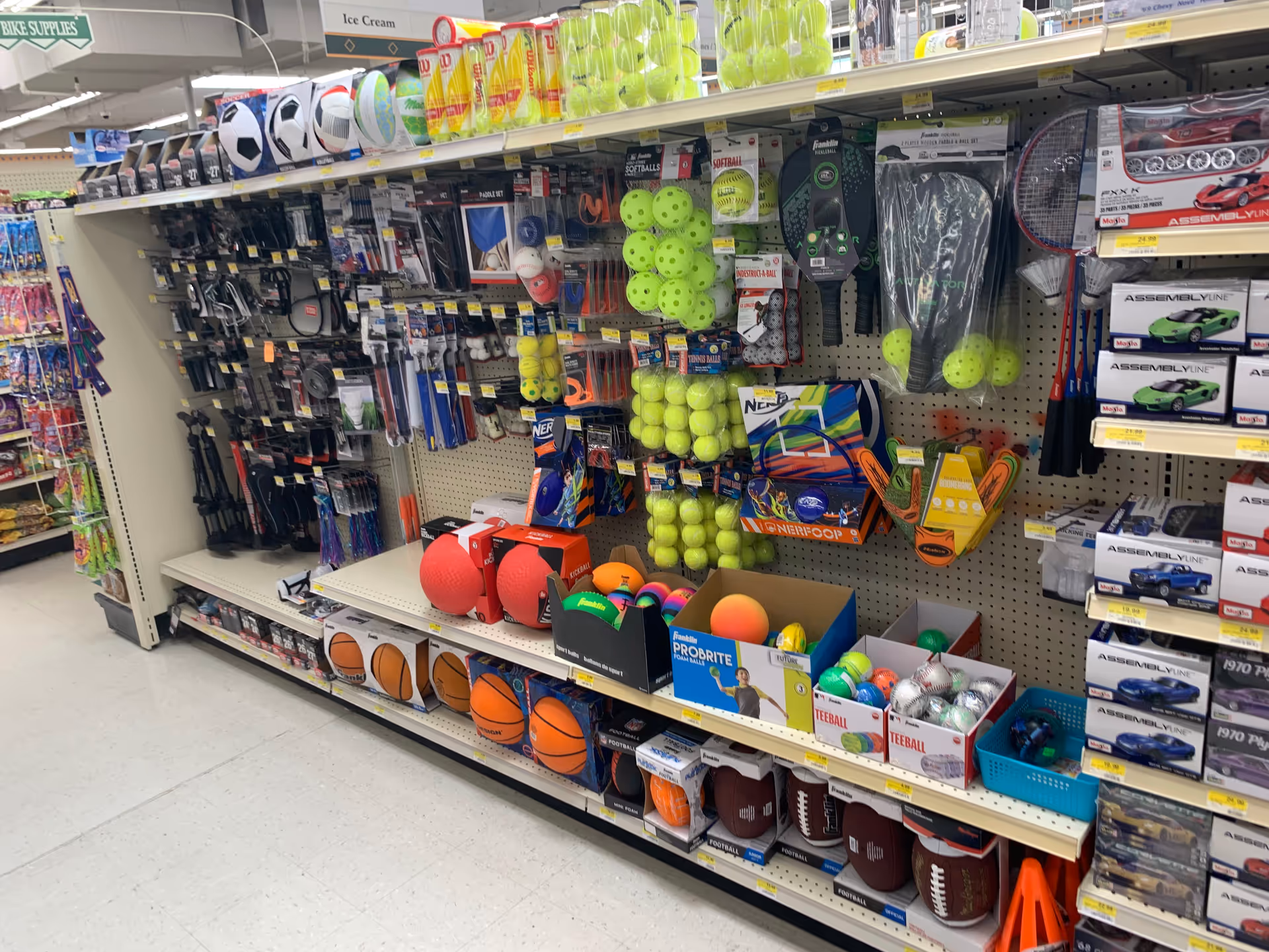A drug store aisle with sports balls and small exercise gear on shelves.