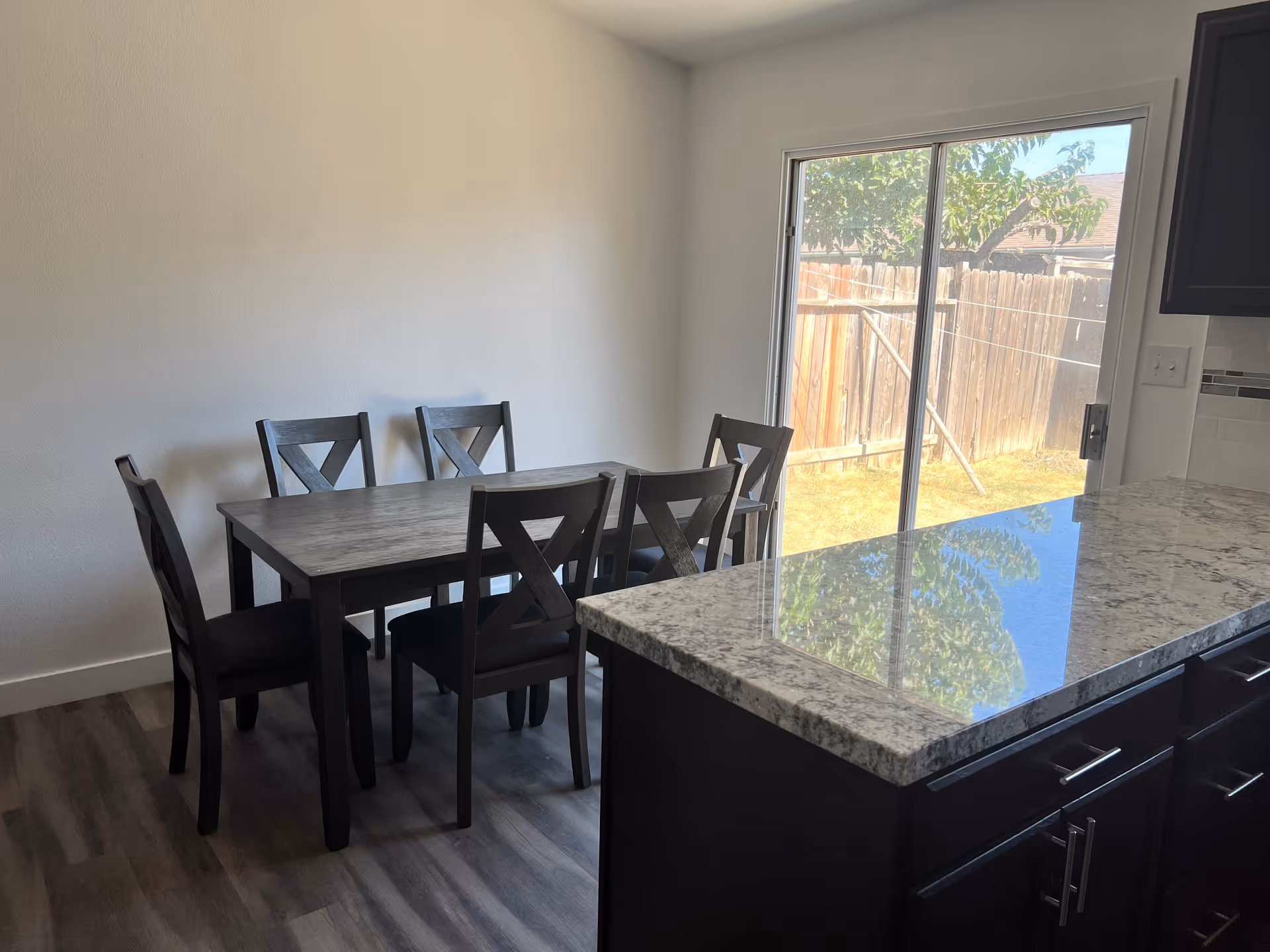 Interior dining area with a table, six chairs, and a granite island near a sliding door.