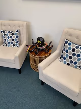 Two beige armchairs with blue patterned cushions sit beside a round wicker table.