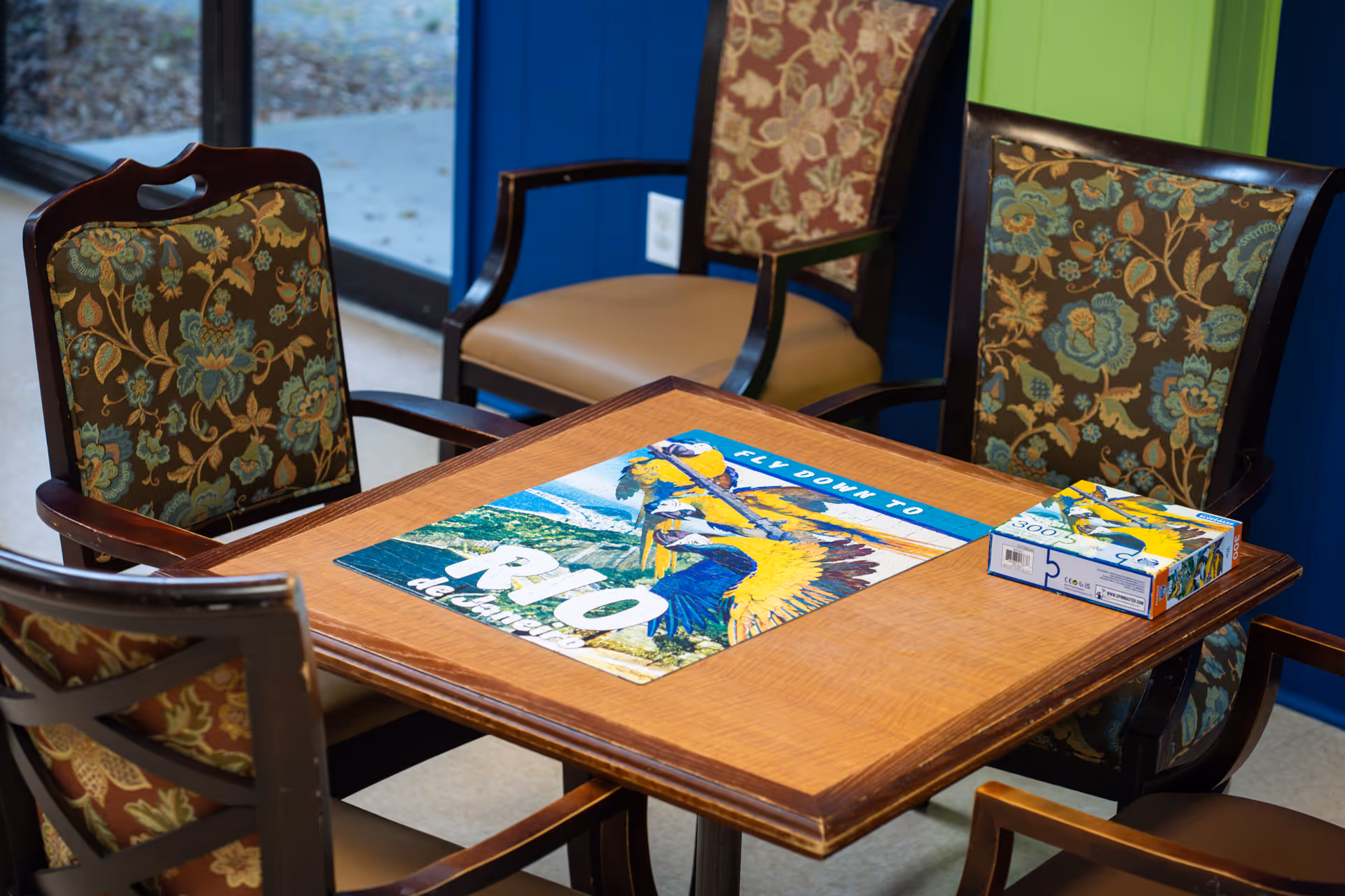 Indoor seating area with a wooden table, floral chairs, and a puzzle box.