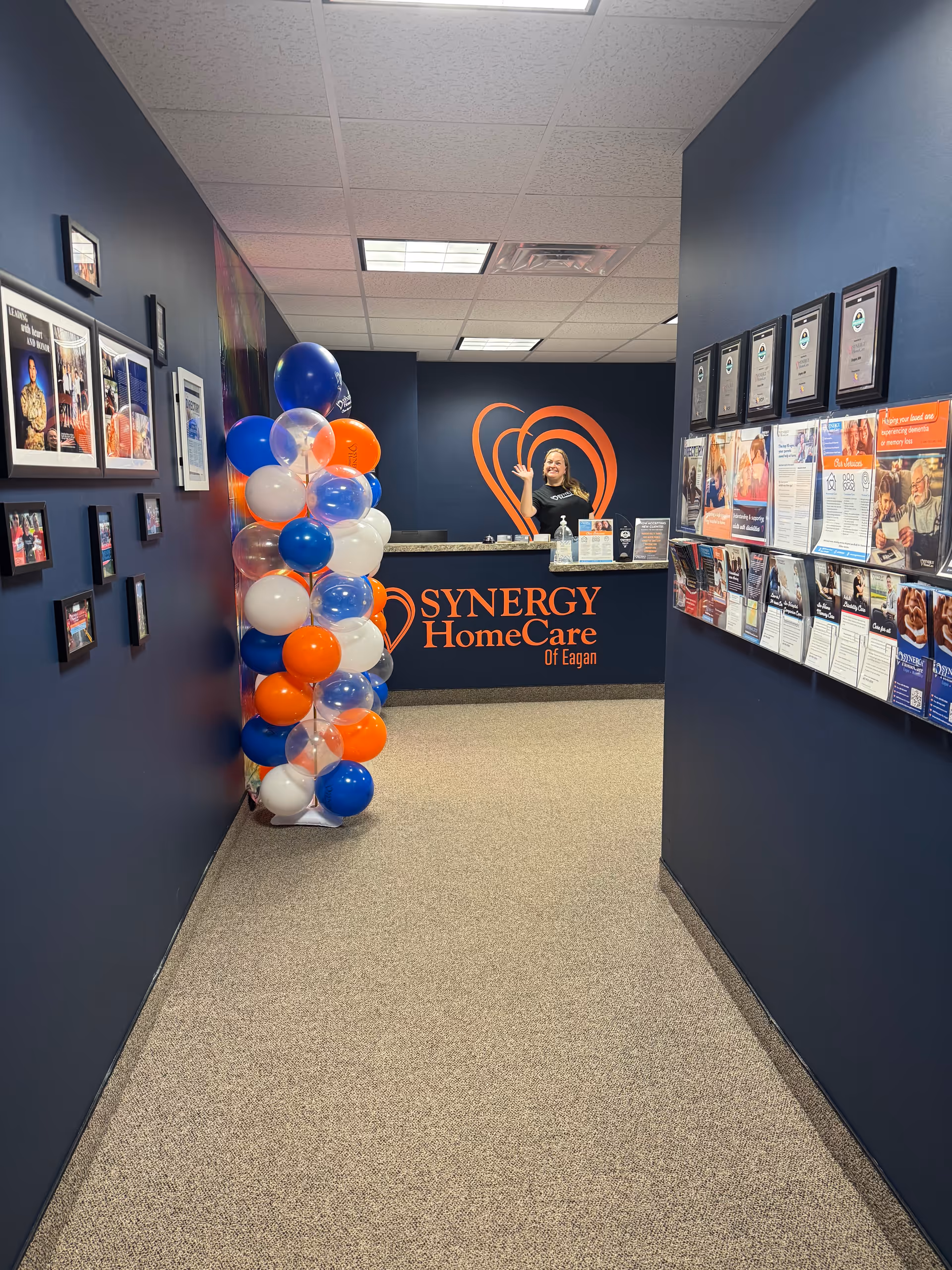 Navy hallway leading to a reception desk with SYNERGY HomeCare branding and balloon decor.