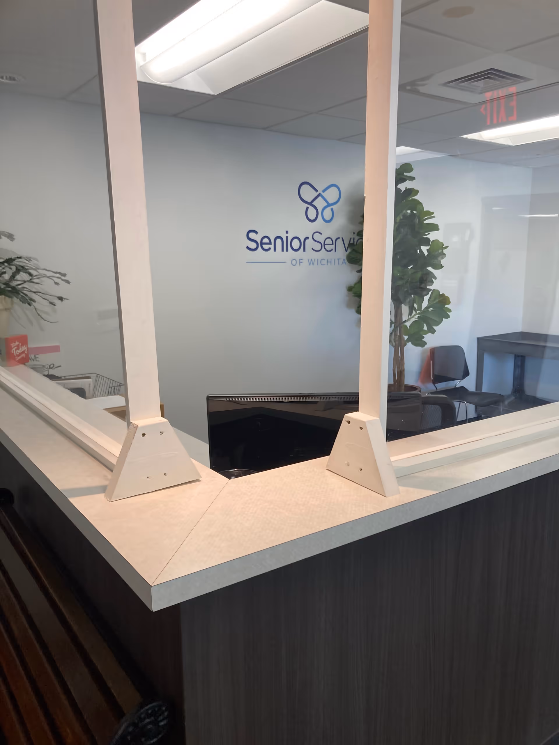 Reception desk with glass partition and Senior Services of Wichita logo on wall.