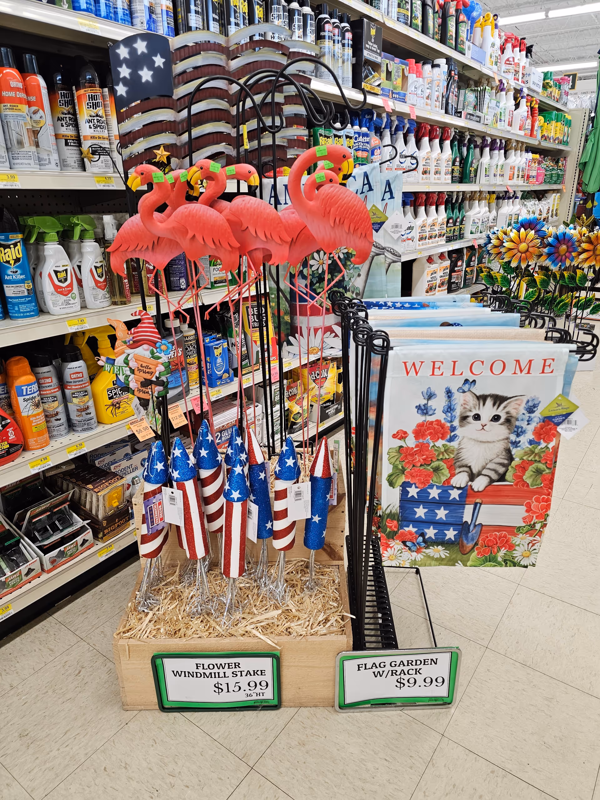 A retail aisle displays patriotic decorations, flamingo yard stakes, and a Welcome sign.