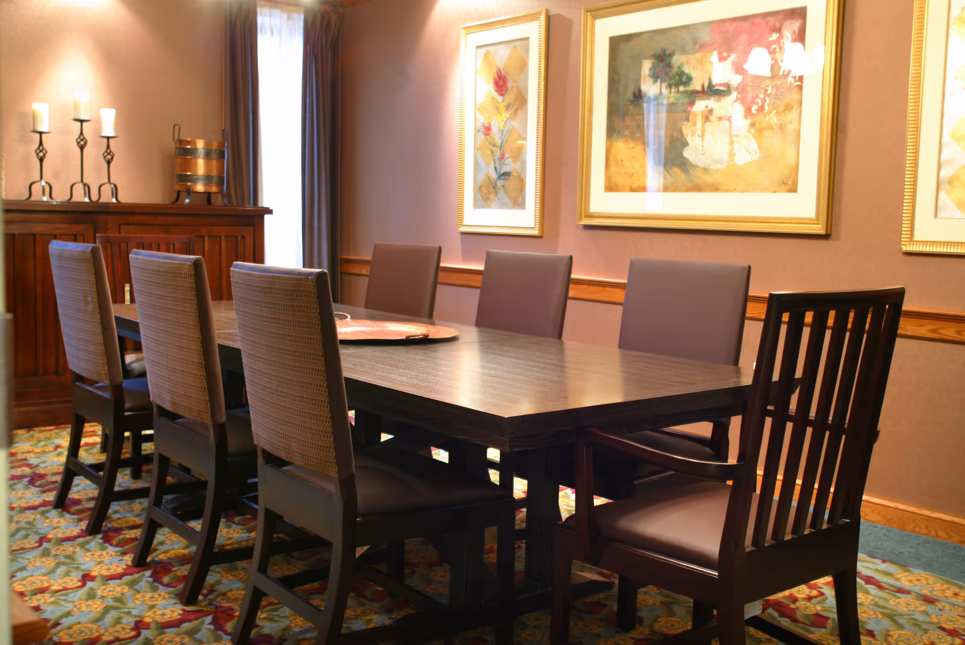 A long dining table with chairs in a warmly lit senior living dining room.