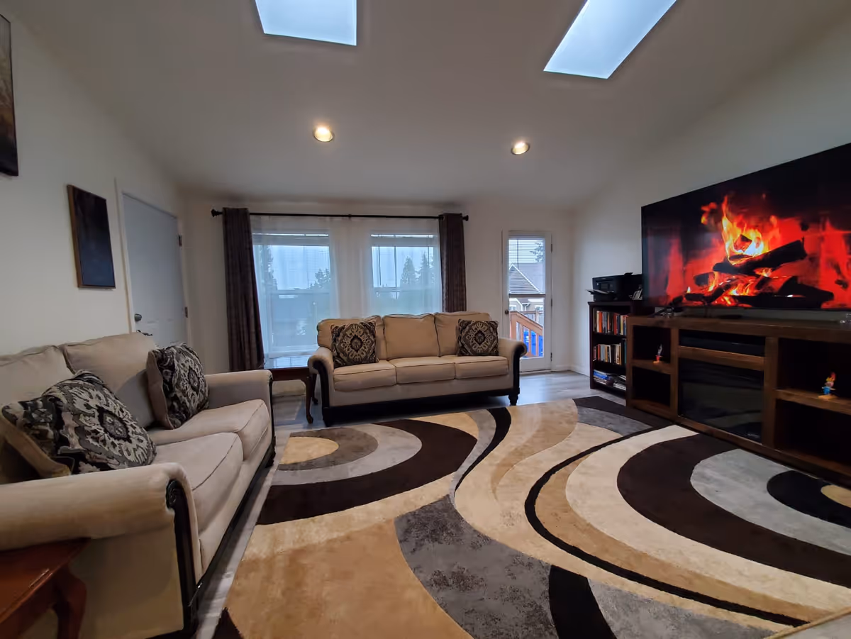 Cozy living room with beige couches, a patterned rug, and a large TV.