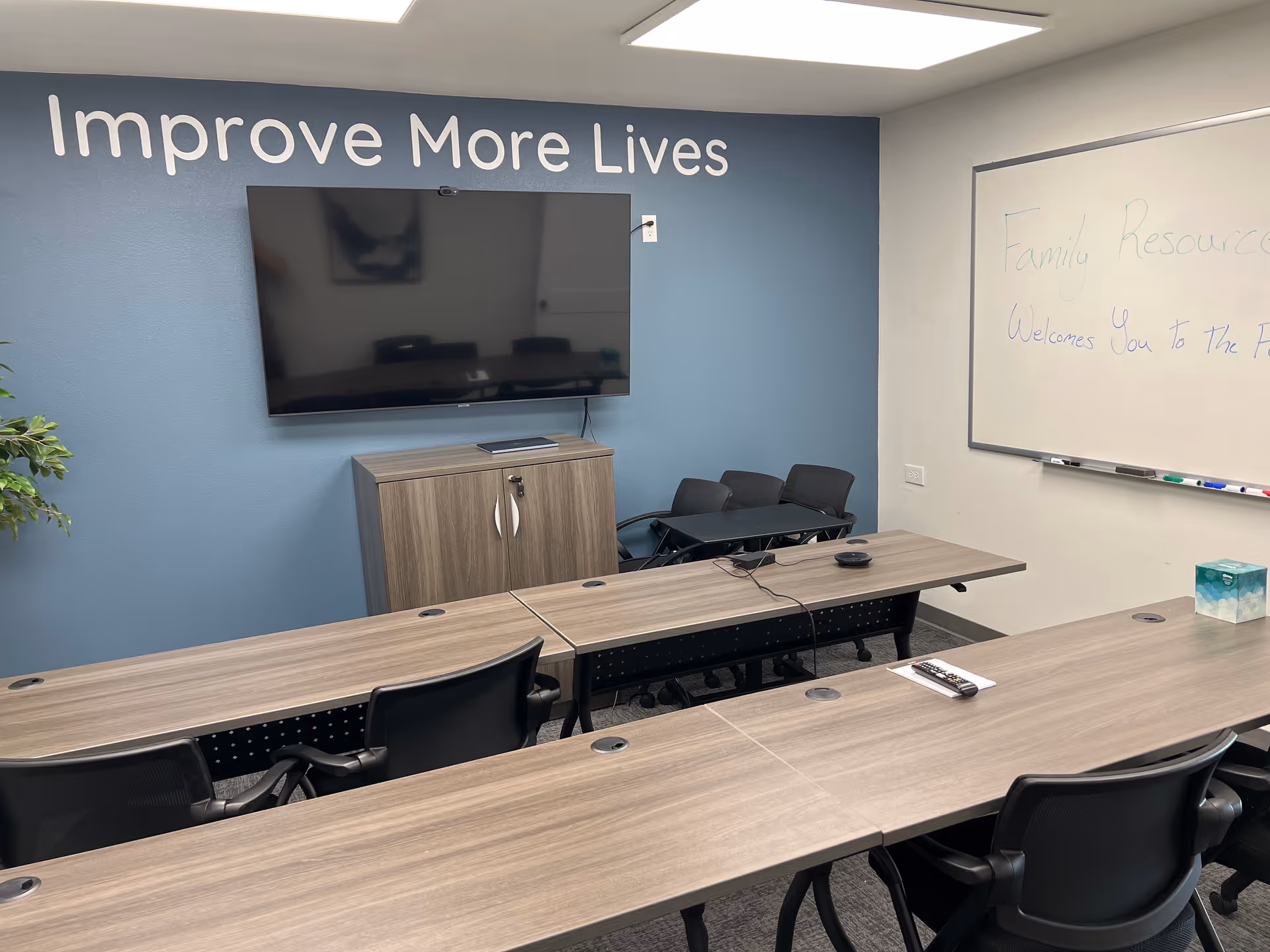 A training conference room with a TV, whiteboard, and long desks in a blue-walled space.