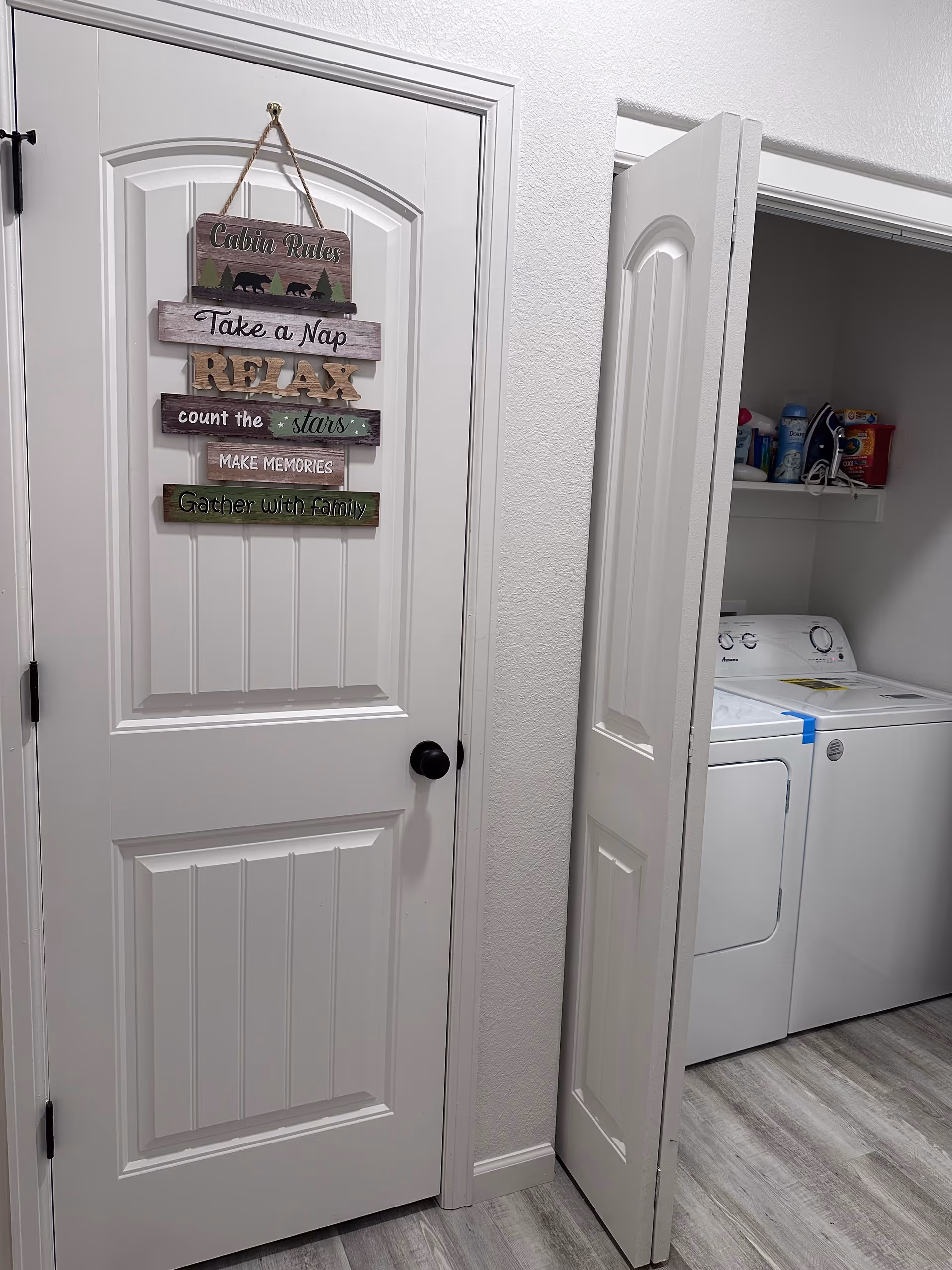 White interior door with decorative sign beside an open laundry closet housing a washer.