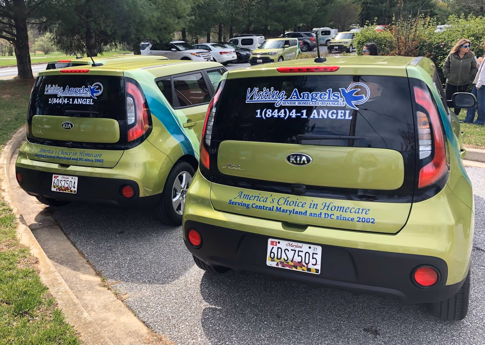 Two lime-green Visiting Angels vehicles parked in a lot at Annapolis with people nearby.