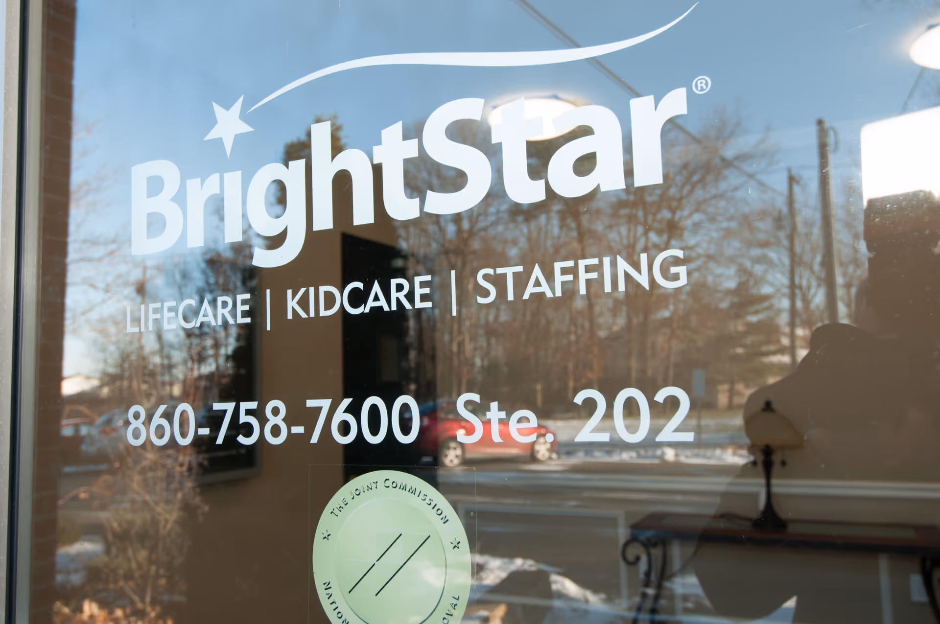 BrightStar Care storefront window with logo and phone number, street reflection