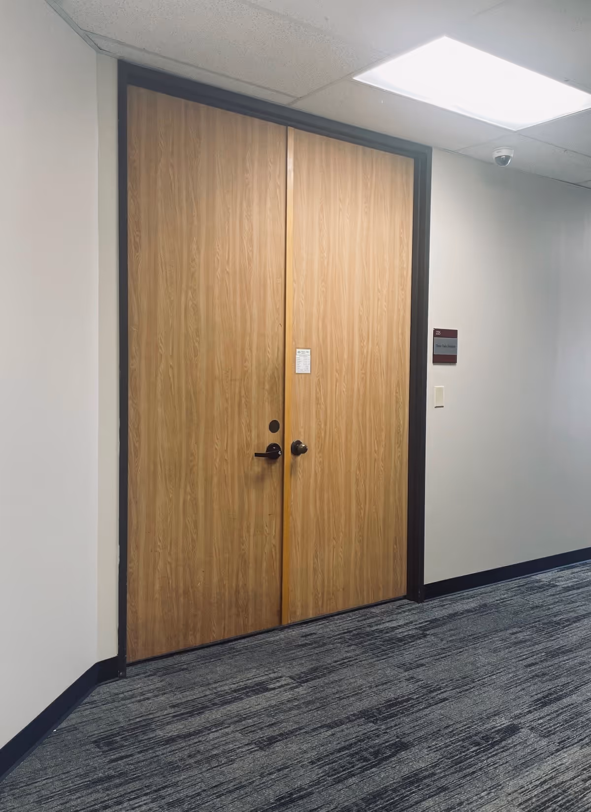 Wooden double doors along a carpeted hallway inside a facility.
