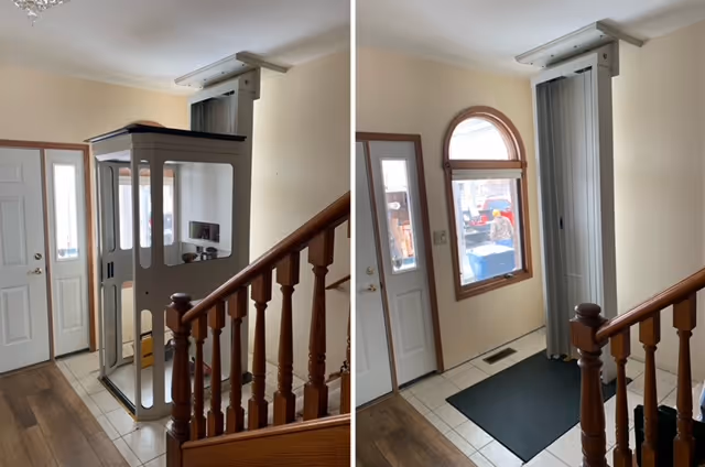Indoor entry area with a vertical platform lift beside a wooden staircase railing.