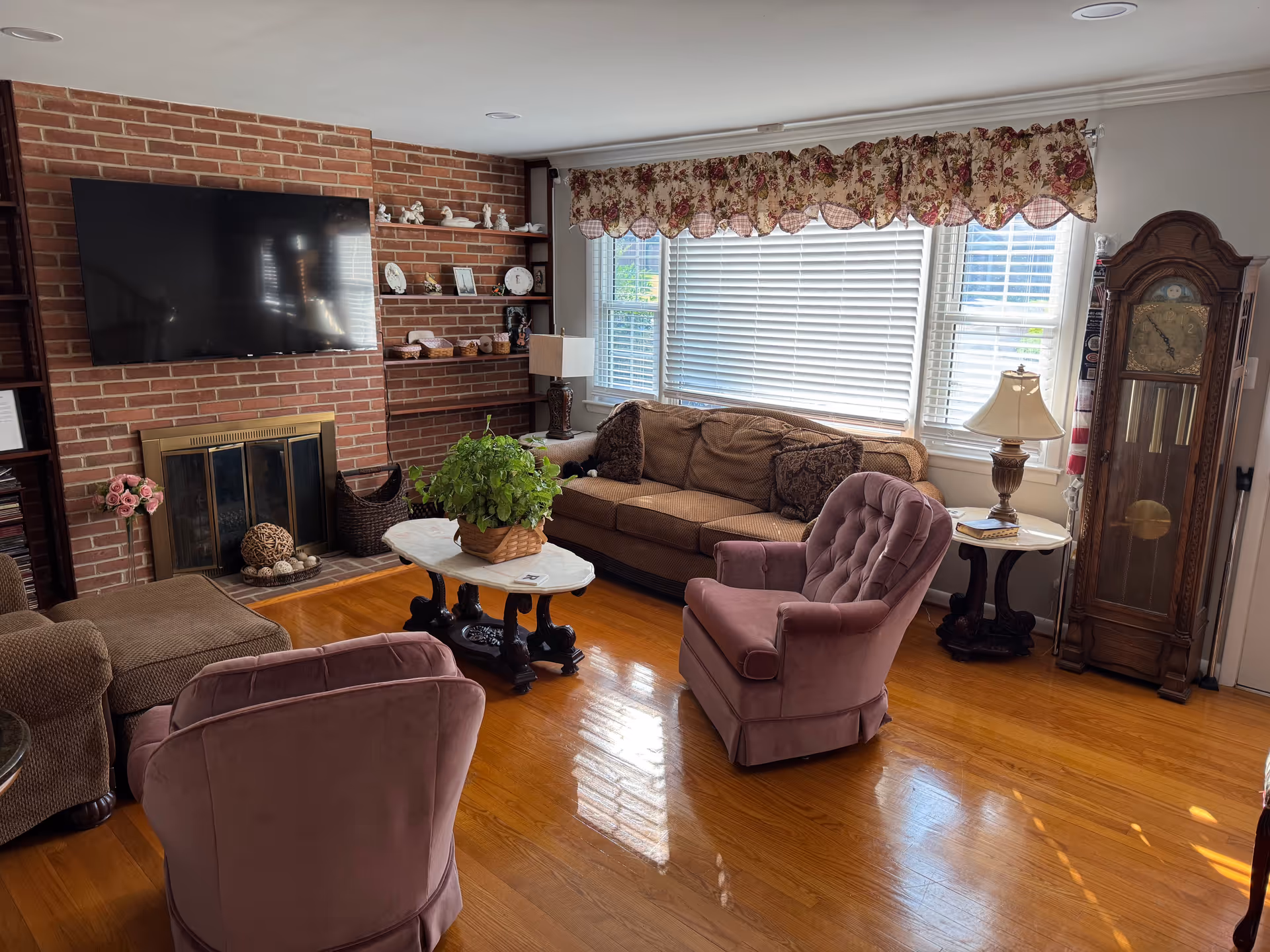 Cozy living room with brick fireplace, TV, sectional sofa, and large bright windows.