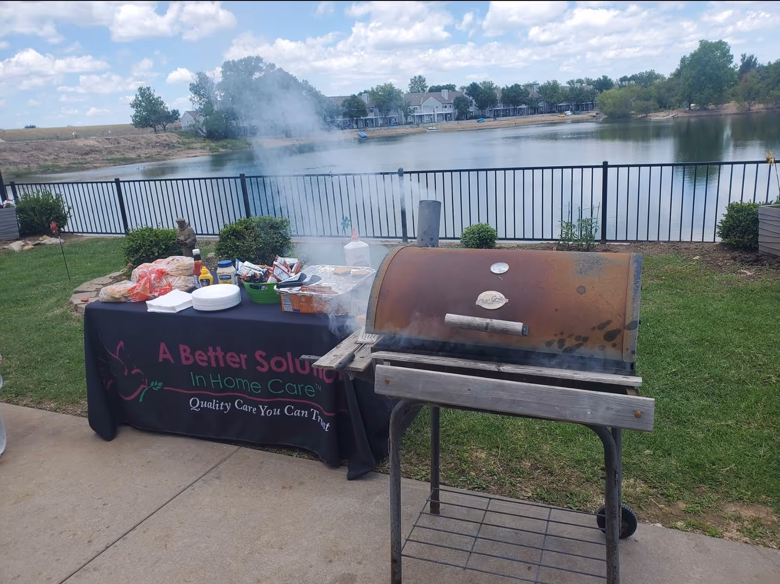 Outdoor barbecue setup beside a lake with a food table and grill.