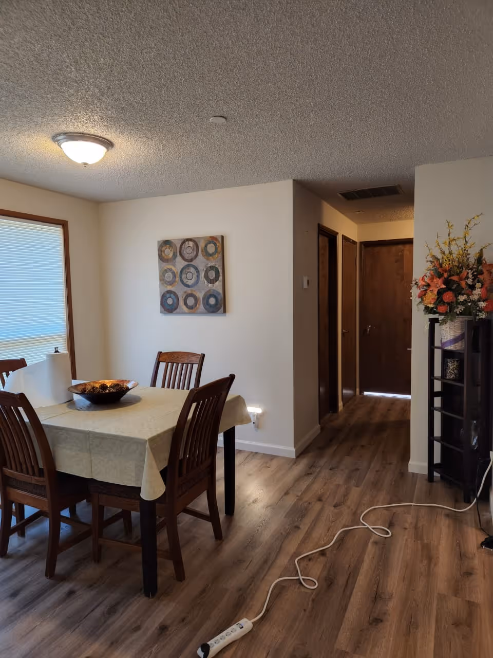 A dining room in a senior living facility with a four-seat table and hallway nearby.