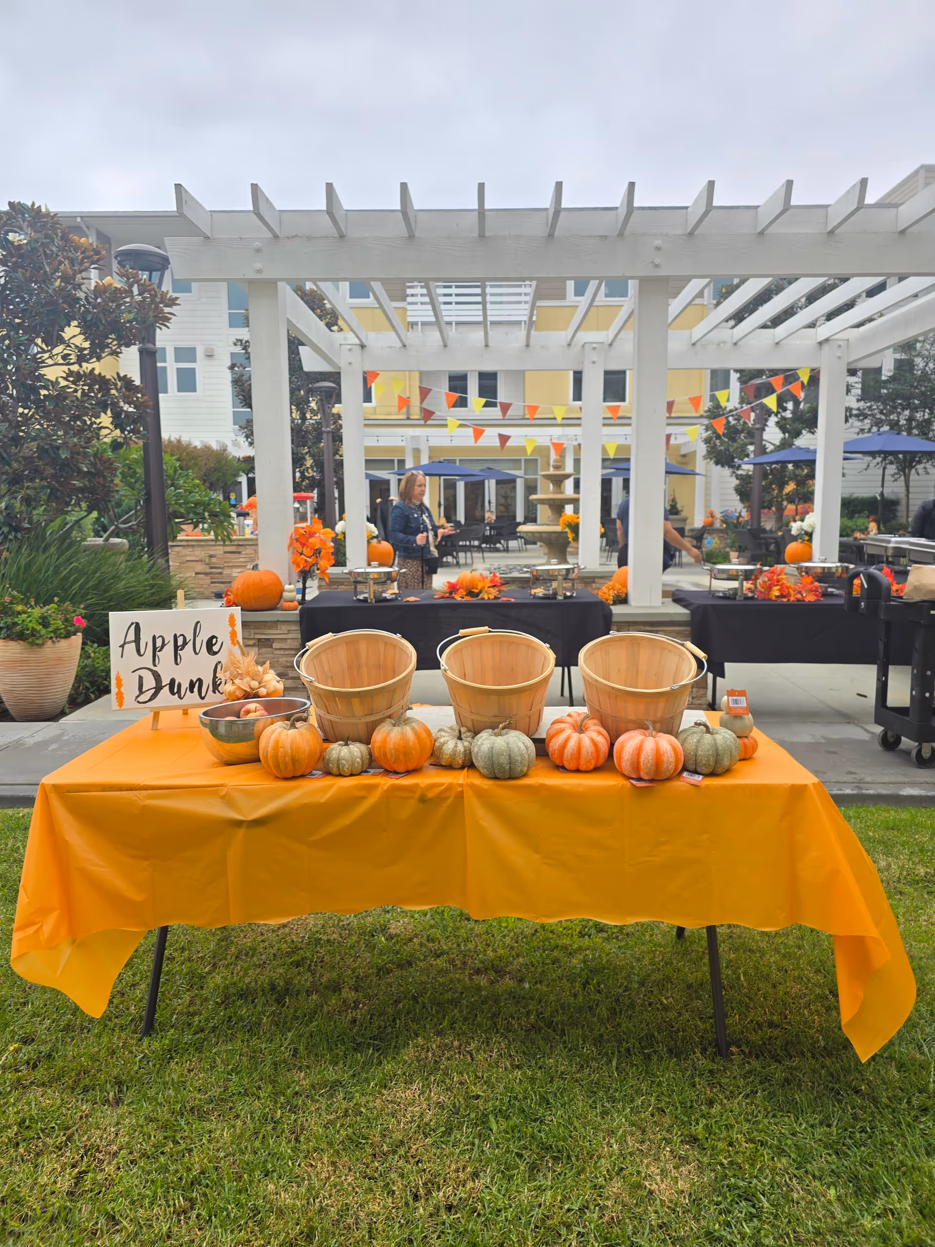 Outdoor courtyard setup with orange-draped table, pumpkins, bunting, and people in background.